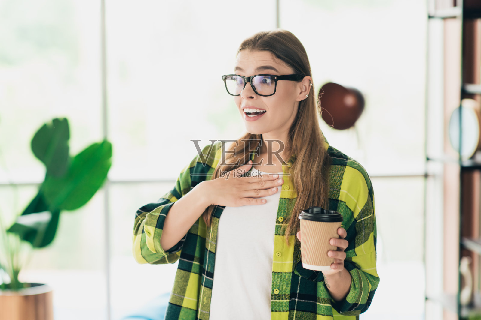 迷人的女性在时尚的室内空间中手握咖啡杯，感到兴奋和富有表现力，享受学习间歇。照片摄影图片