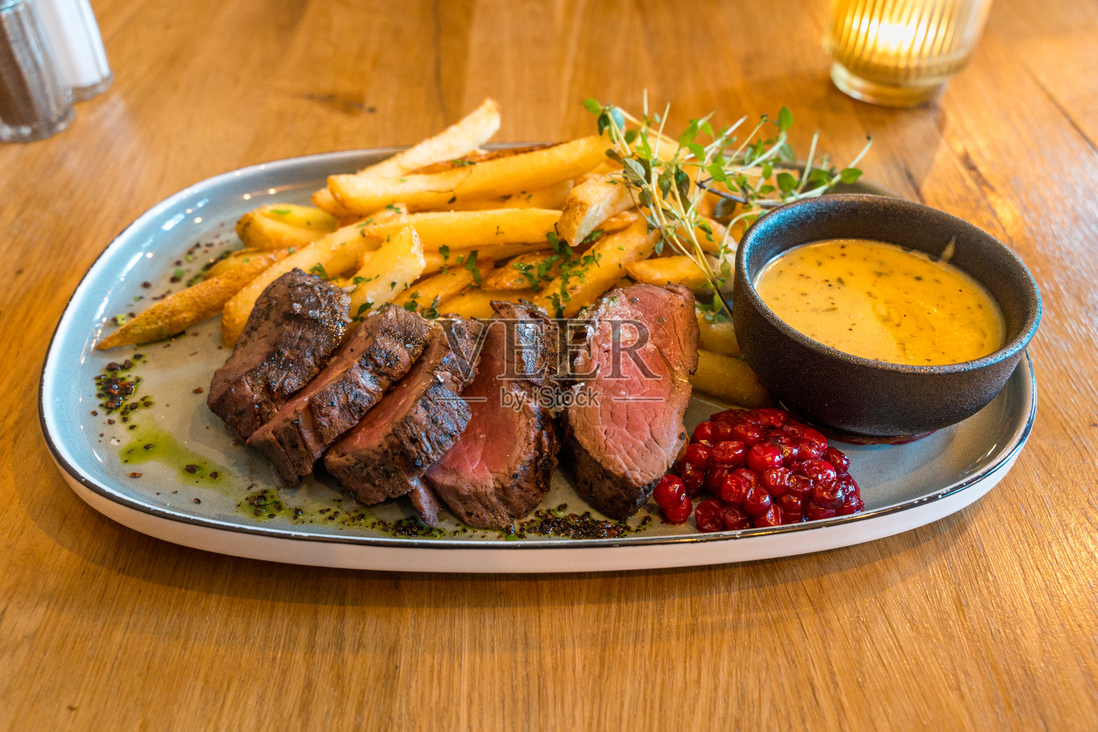 挪威传统美食：中等生熟的驼鹿牛排，切片，撒上海盐和胡椒，配以特制香草酱，旁边有薯条。照片摄影图片