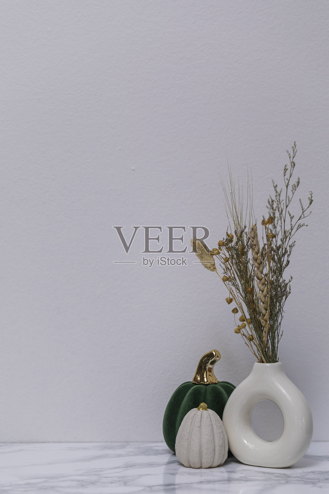 时尚的季节性静物，带有中性色调的陶瓷花瓶，里面装满了干草和深绿色与柔和奶油色的南瓜，适合感恩节和温馨家居室内的秋季主题构图。照片摄影图片