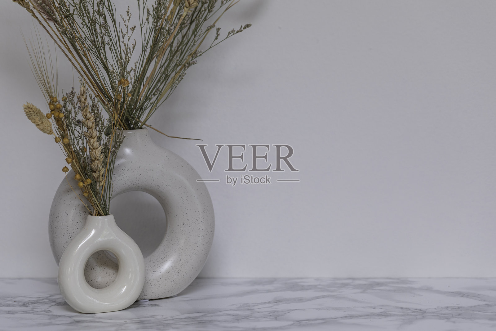 优雅的斯堪的纳维亚风格装饰场景，圆形陶瓷花瓶中插着干燥的小麦和草茎，放置在大理石桌面上，背景中性，适合极简和现代室内设计。照片摄影图片