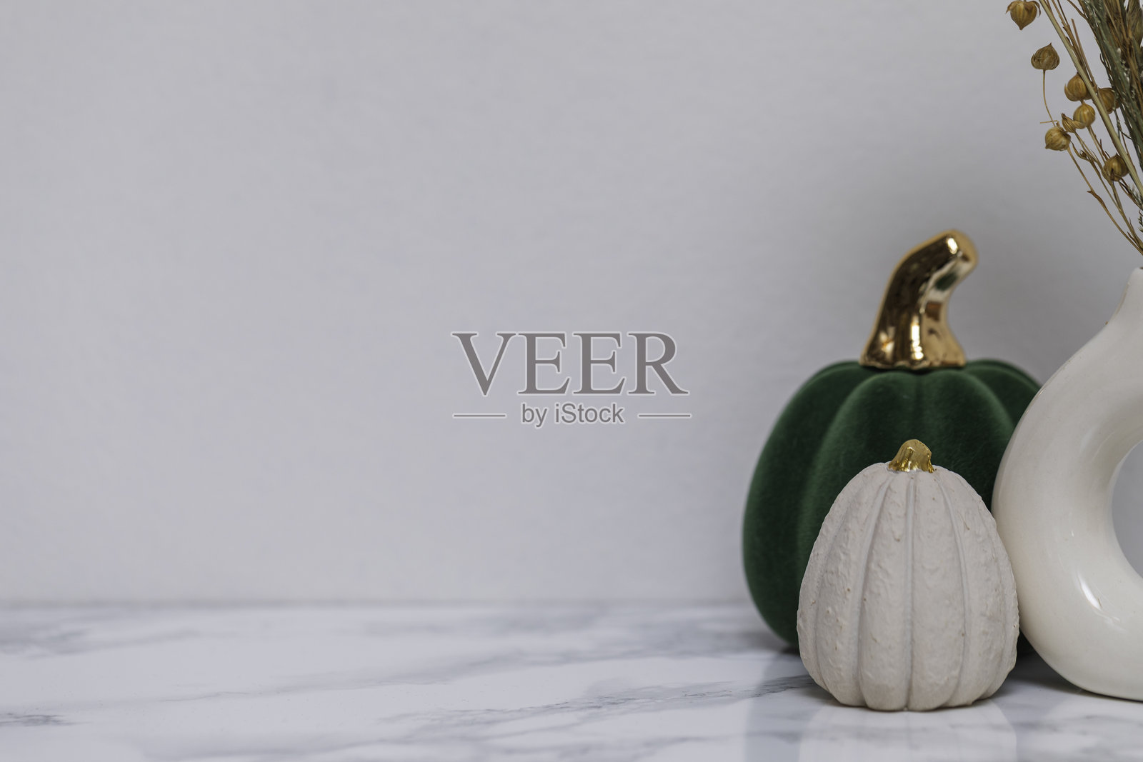 温馨的秋季家居装饰，包含两个绿色和奶油色调的装饰南瓜，金色细节，以及部分陶瓷花瓶，背景为大理石，适合感恩节季节风格。照片摄影图片