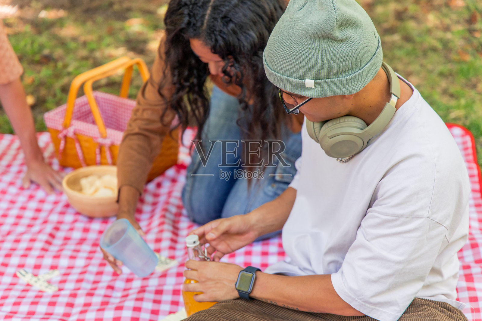 多种族年轻人在公园里打开饮料并准备野餐毯照片摄影图片