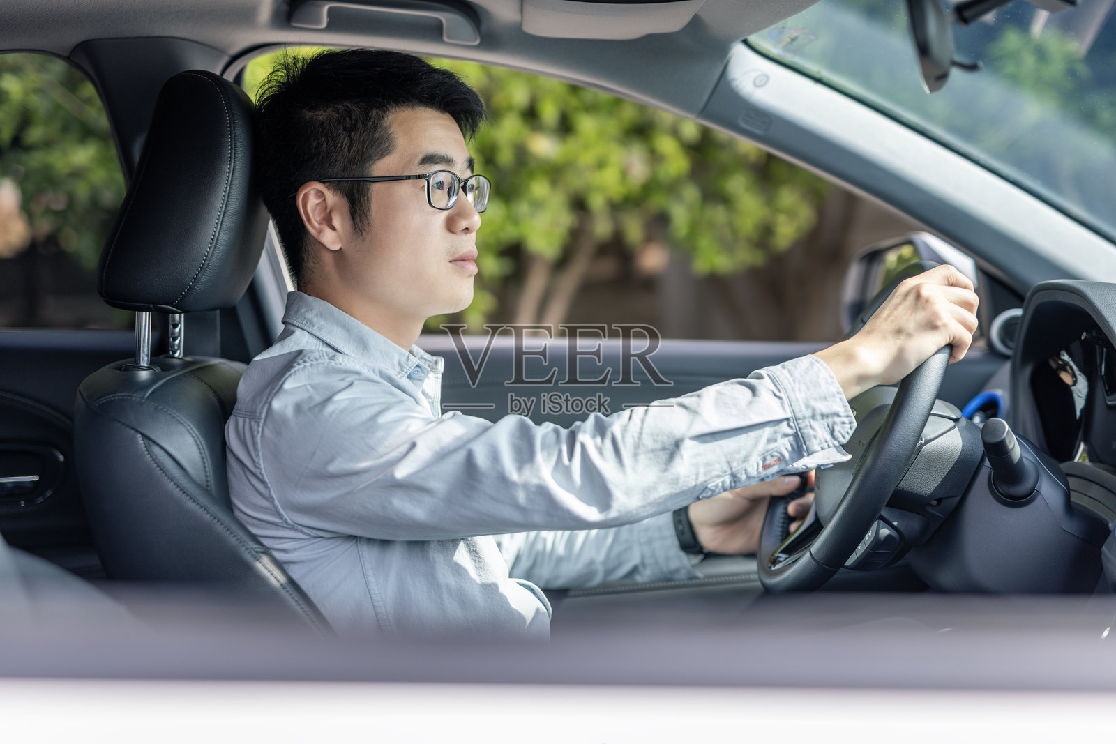 一名戴眼镜、穿着浅色衬衫的男子正在驾驶汽车照片摄影图片