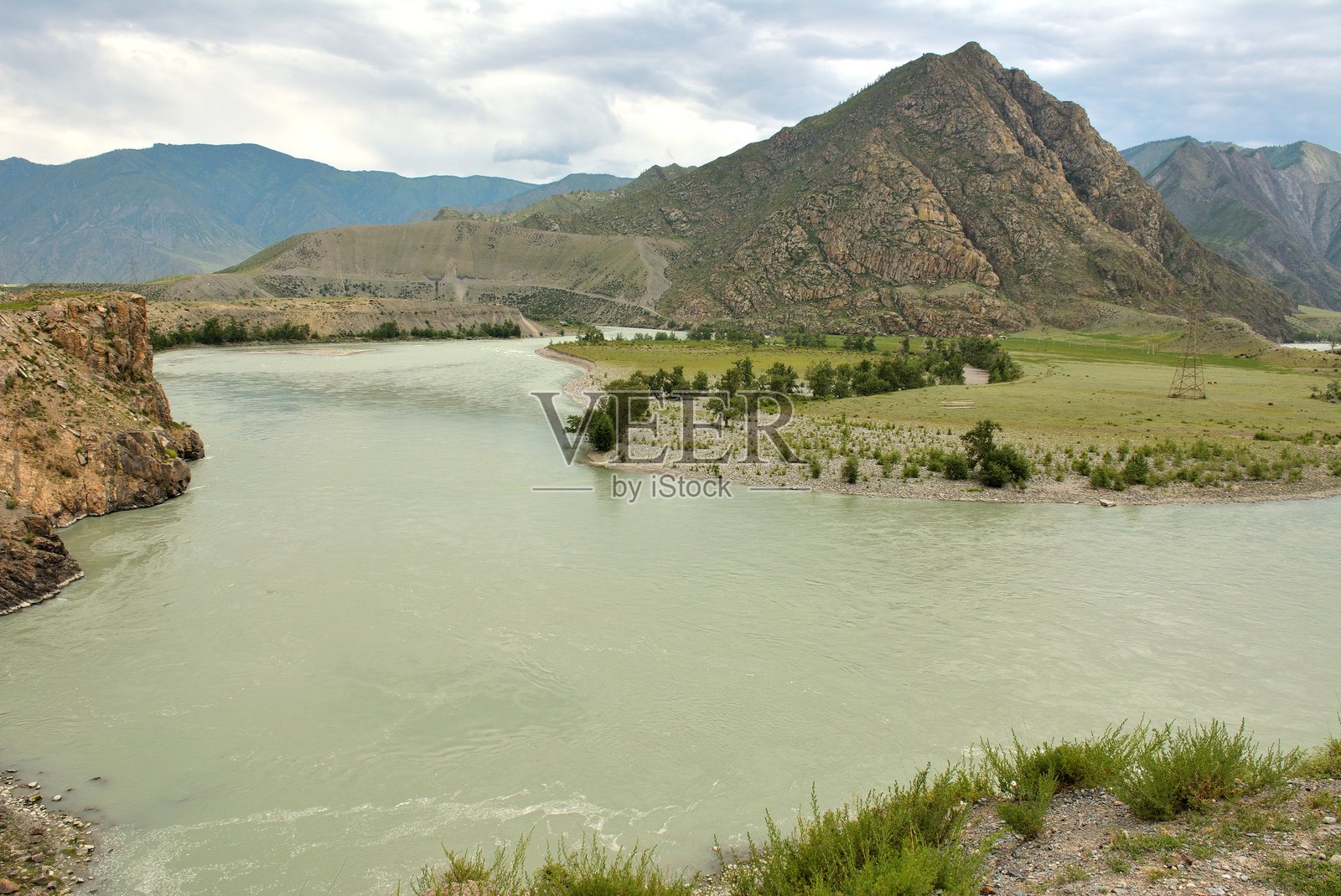 在一个多云的夏日，宽阔而湍急的河流在峡谷中急转弯，四周被高山环绕。照片摄影图片