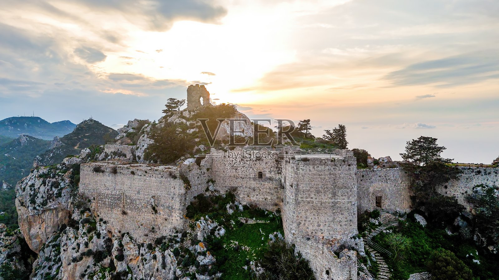 北塞浦路斯山脊上的历史悠久的中世纪坎塔拉建筑的日落航拍图，古老的石头遗迹被郁郁葱葱的绿树环绕，风景如画的景观，天空壮观，海岸线全景尽收眼底。照片摄影图片