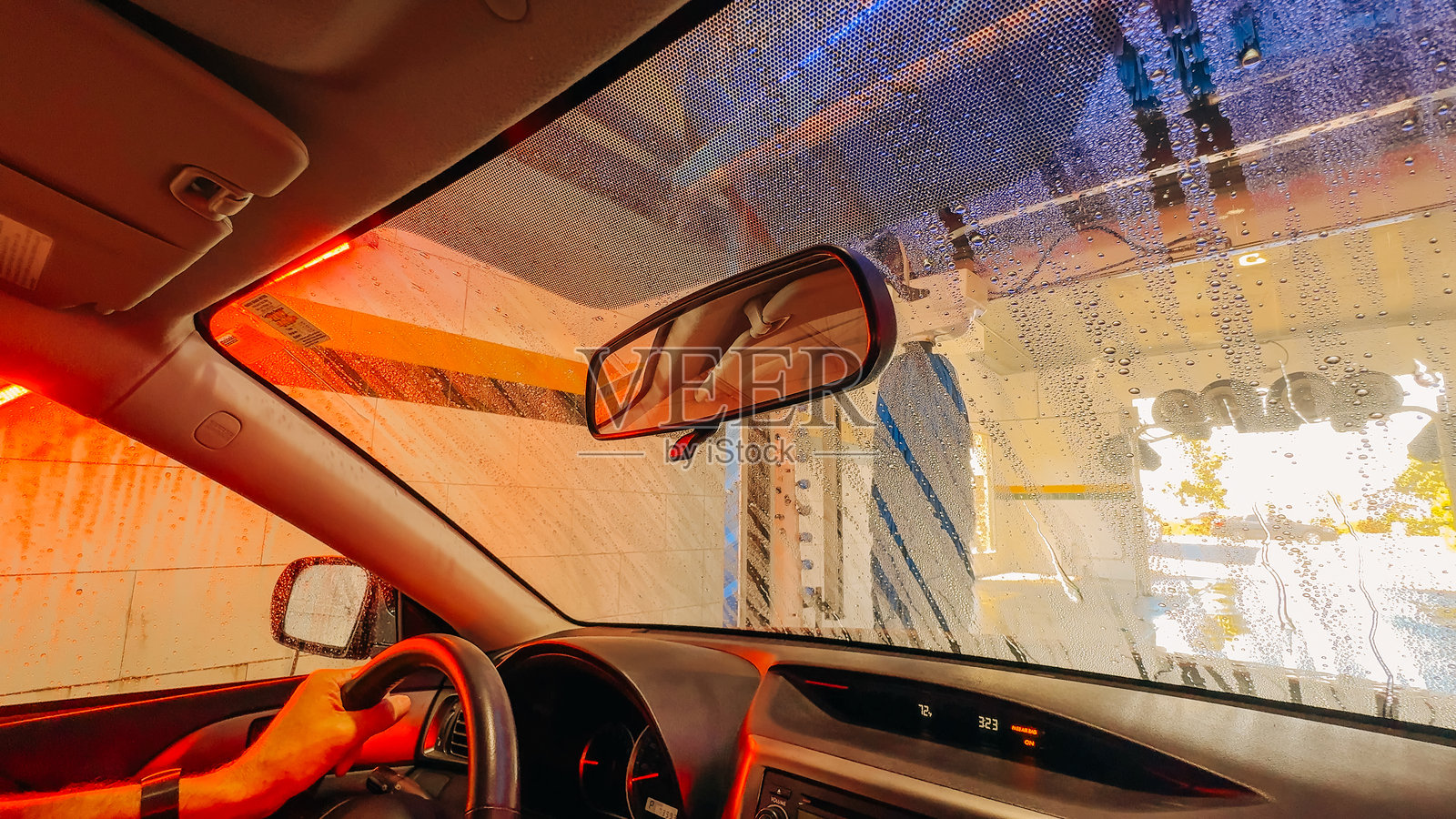 一个人驾驶着汽车经过自动洗车机，肥皂和水流淌在挡风玻璃上。照片摄影图片