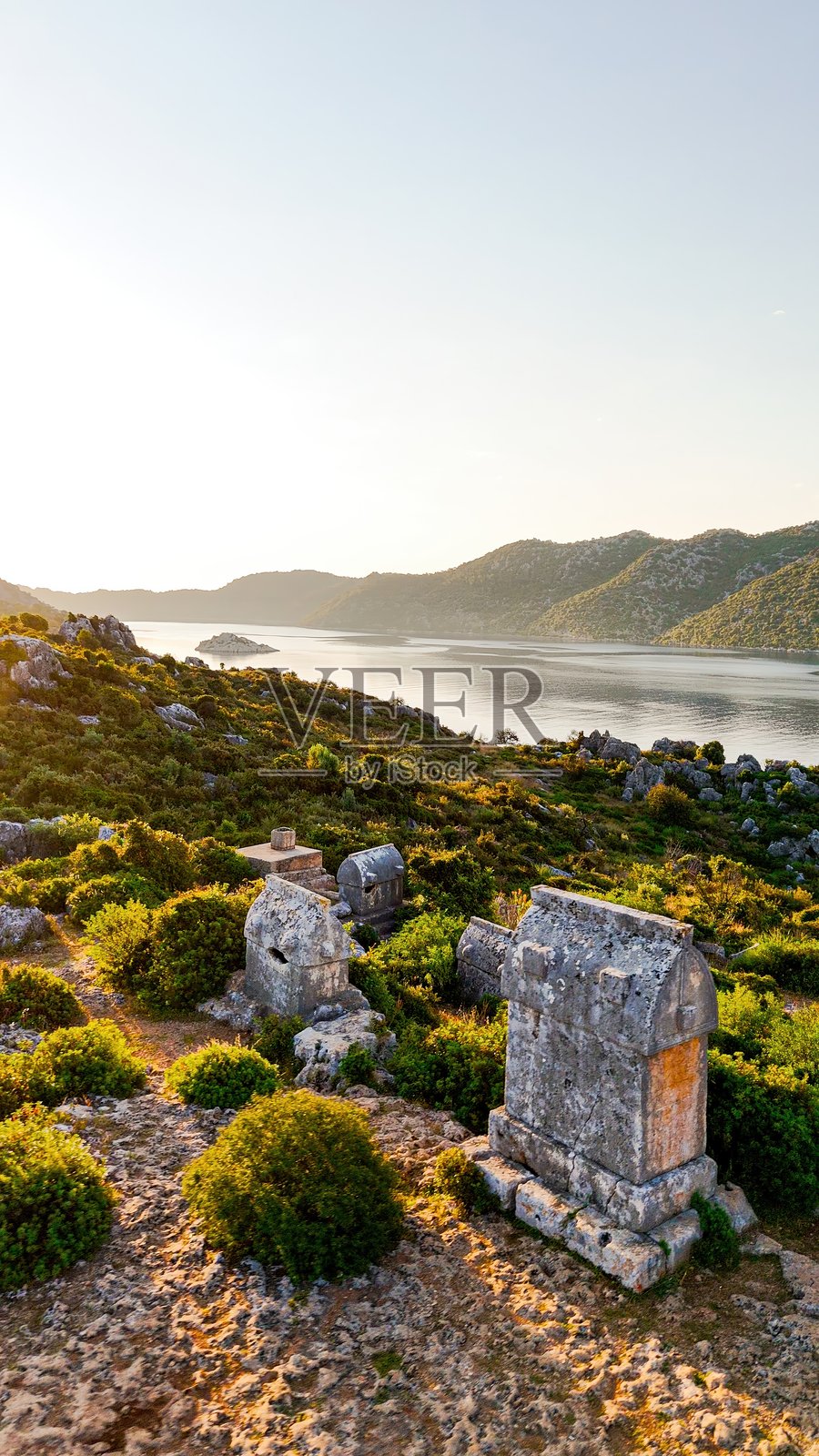 凯科瓦宁静海面上方山坡上的黎基亚岩墓日出鸟瞰，周围环绕着郁郁葱葱的地中海植被和海岸风光，文化遗产与历史旅游概念照片摄影图片