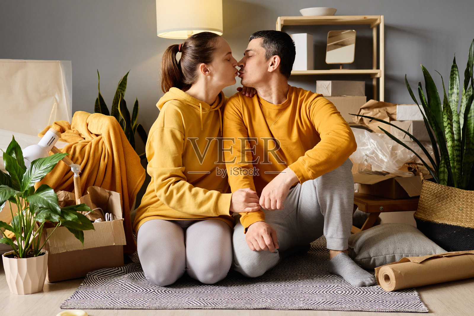 快乐的情侣在新家庆祝，互相亲吻，周围是搬家的箱子和家居植物。照片摄影图片