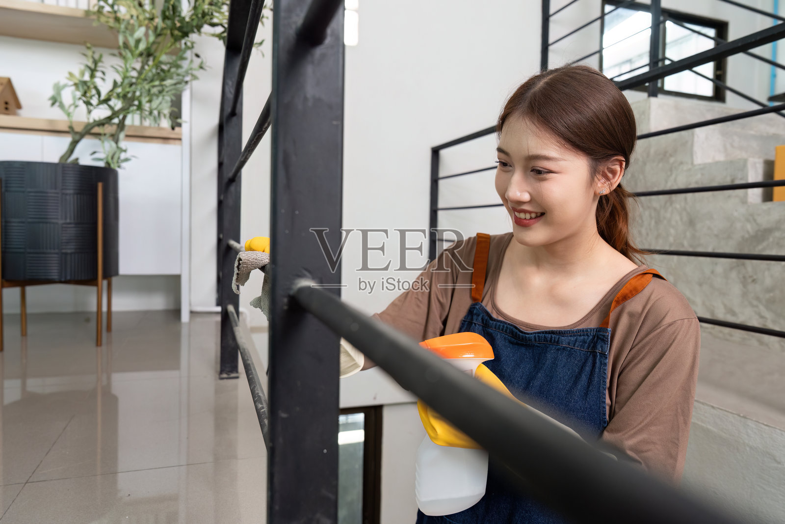 家庭清洁。年轻女性微笑着在室内清洁栏杆。照片摄影图片