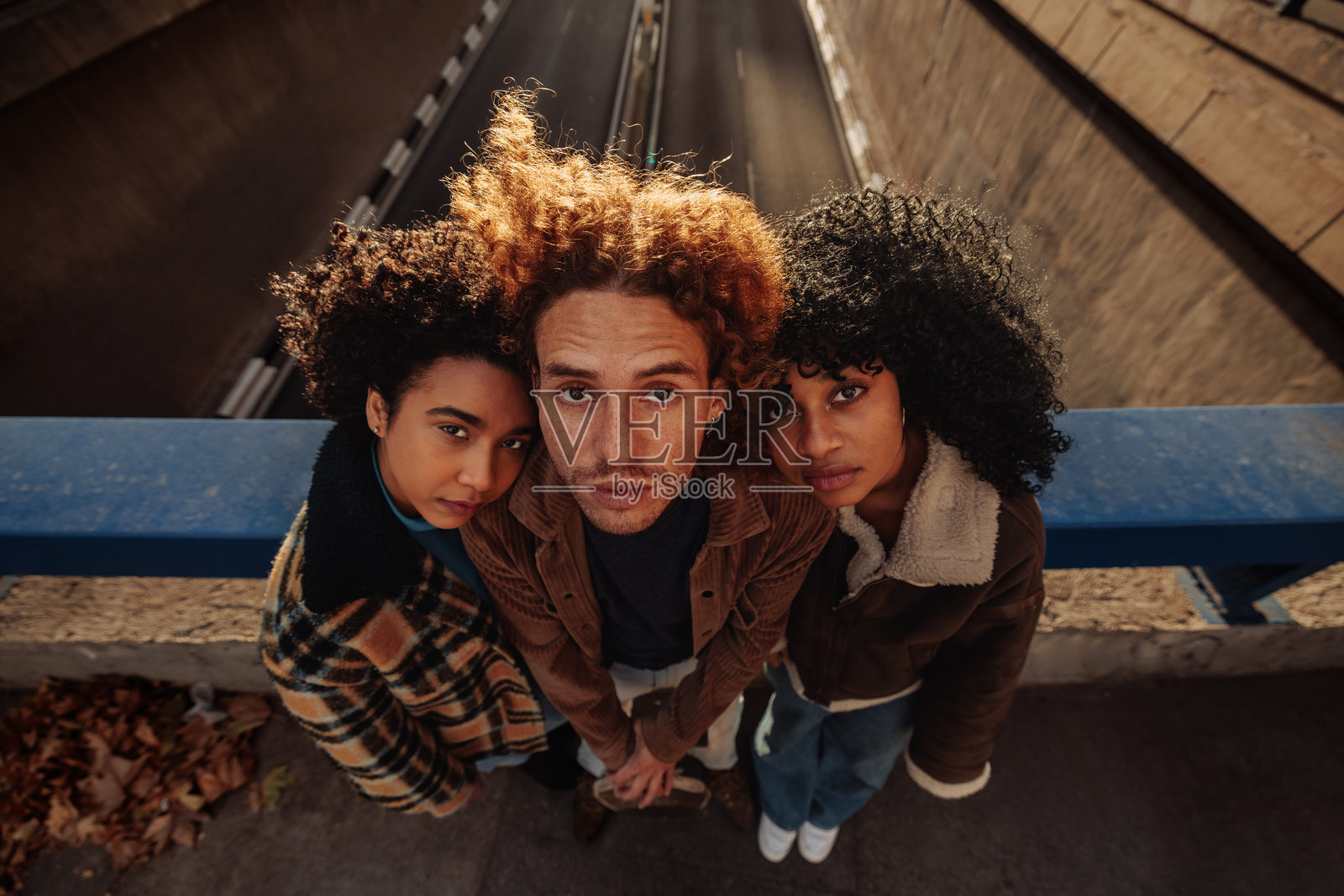 三个年轻朋友靠在桥栏杆上向下看照片摄影图片