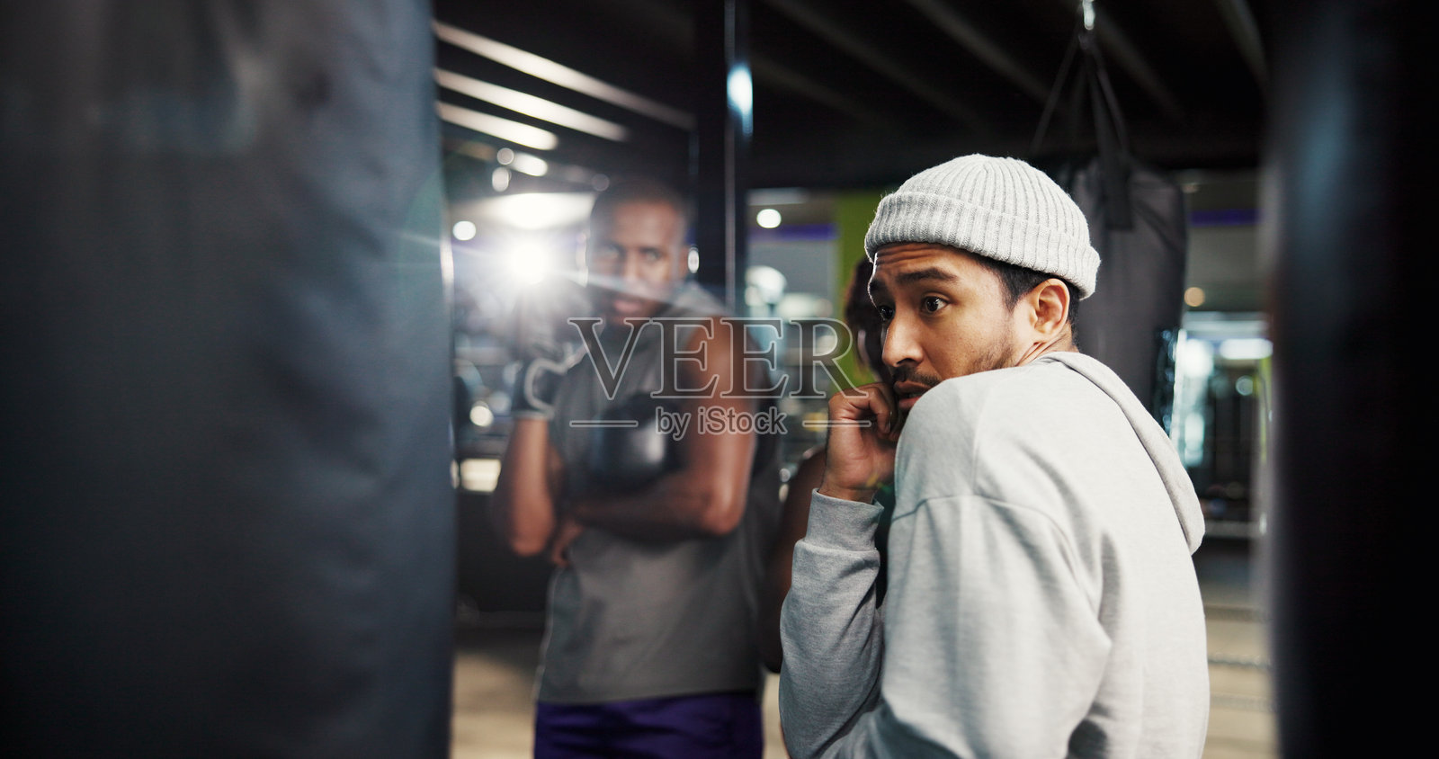 在健身房进行拳击防守训练，教练或运动员在打沙袋的团体课程中进行指导，学习战斗技巧和应对体育挑战。照片摄影图片