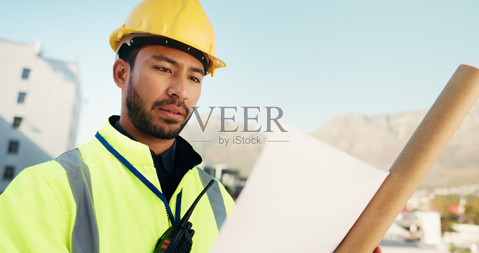 城市中一名男子正在阅读蓝图和工程图，以撰写进度报告，涉及建筑和承包商。户外有个人的平面图、施工现场和建筑进度安排，适用于翻新项目。照片摄影图片