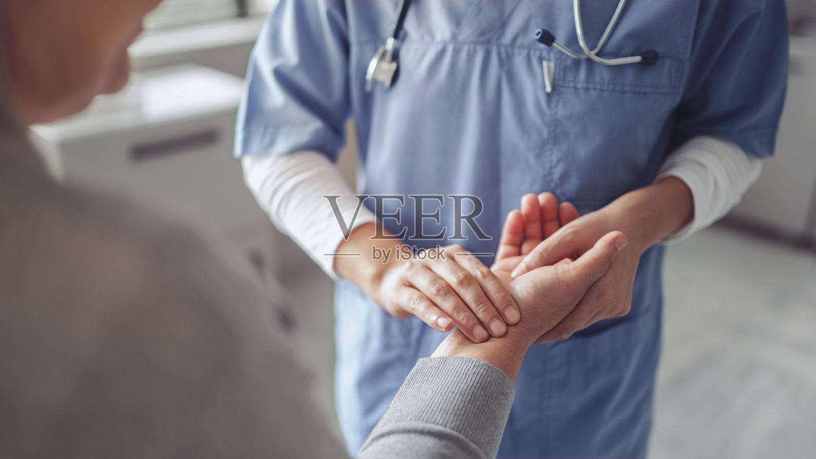 护士握住坐着的老妇人的手，测量她的脉搏。照片摄影图片