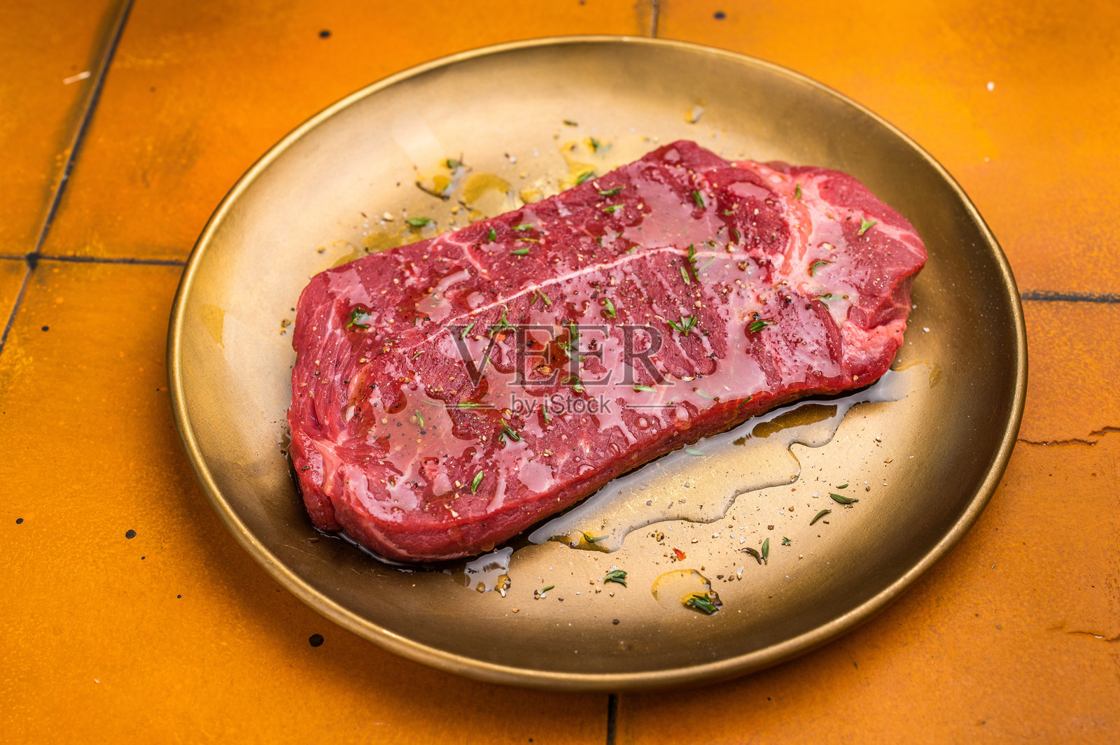 用橄榄油和香草腌制的生顶级西冷牛排或臀部牛排。橙色背景。俯视图。照片摄影图片