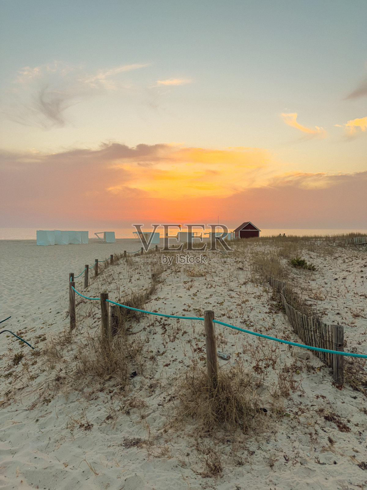 美丽的日落照亮了葡萄牙奥瓦尔的埃斯莫里什海滩沙丘，远处有一条绳索围栏和海滩小屋。照片摄影图片