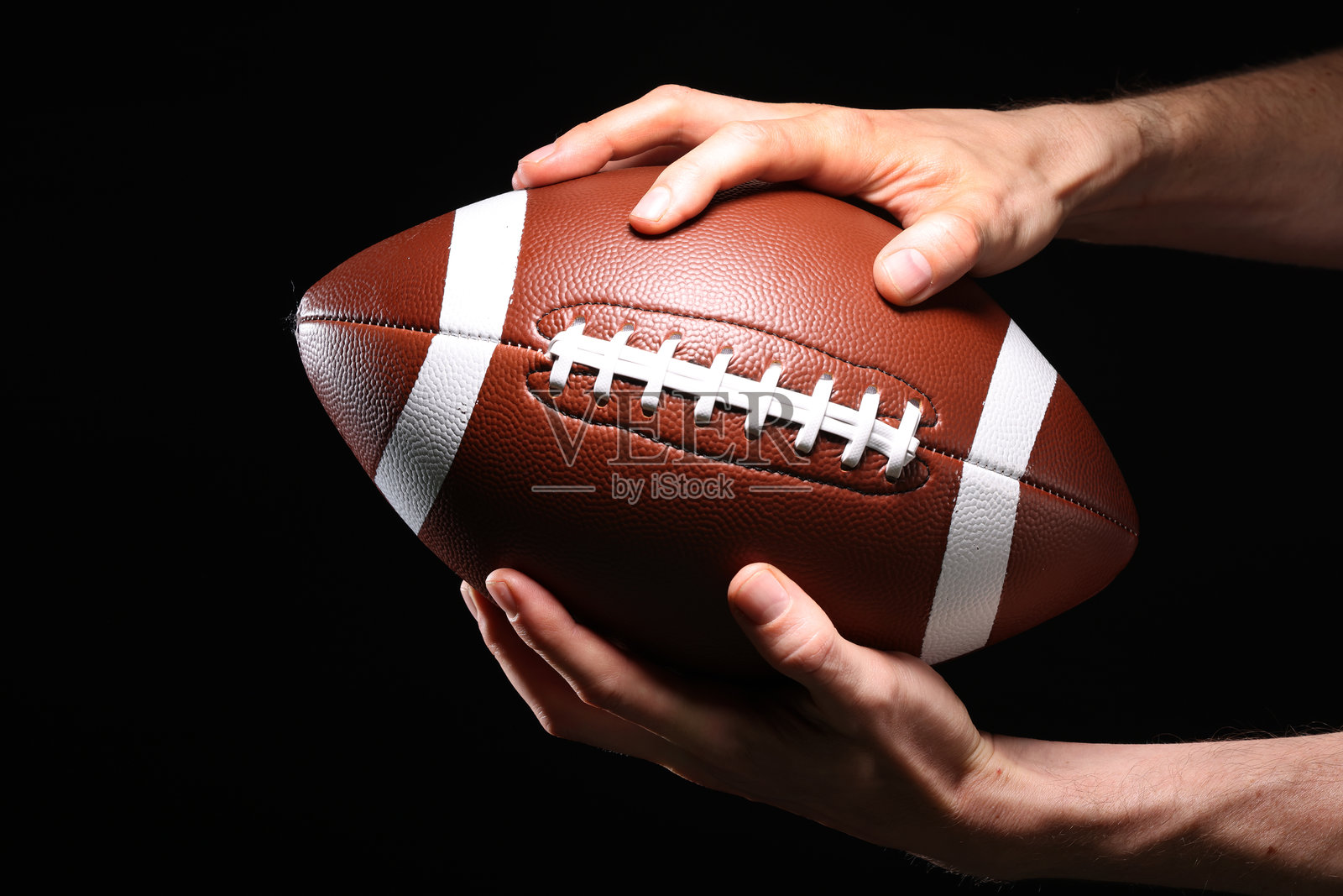 运动员的手特写，举着橄榄球，背景为黑色照片摄影图片