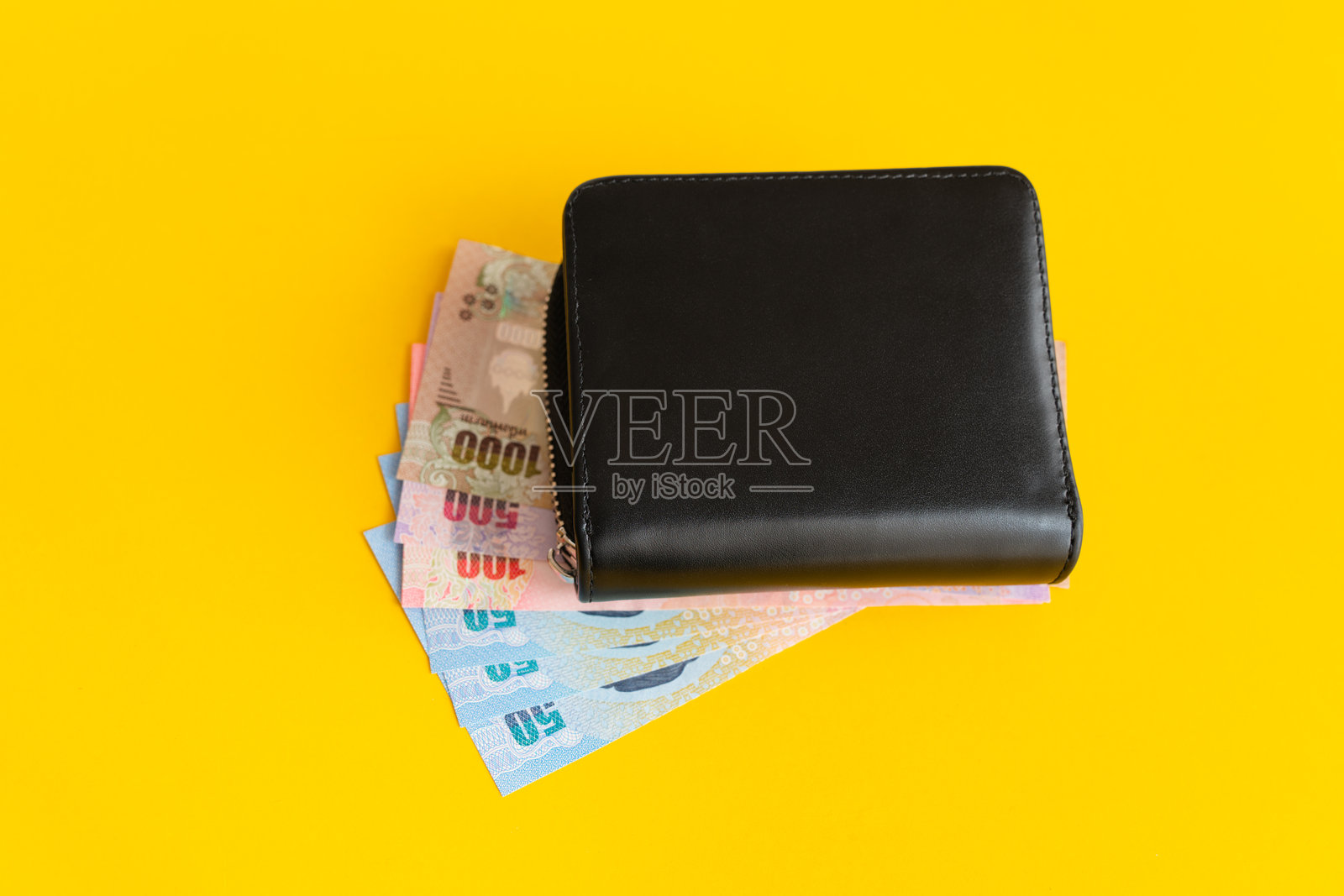 黑色钱包里放着泰国钞票，柔焦效果，背景为黄色。照片摄影图片