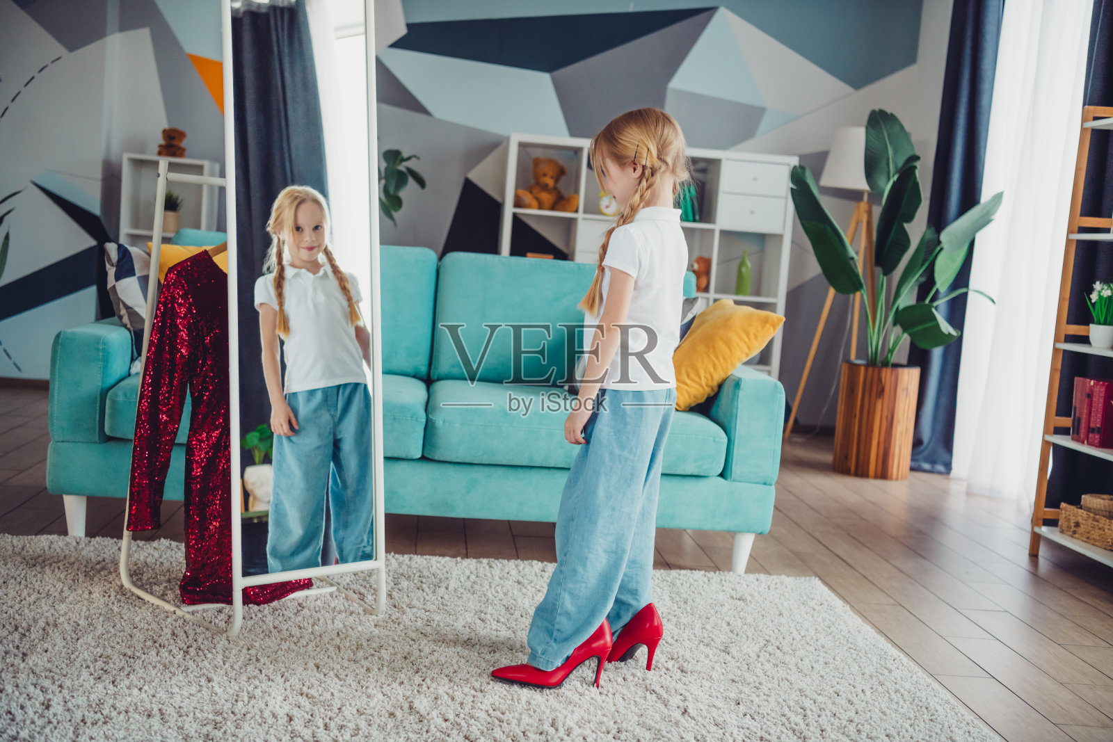 可爱的小女孩在温馨的粉色客厅里试穿红色高跟鞋，扎着辫子。照片摄影图片