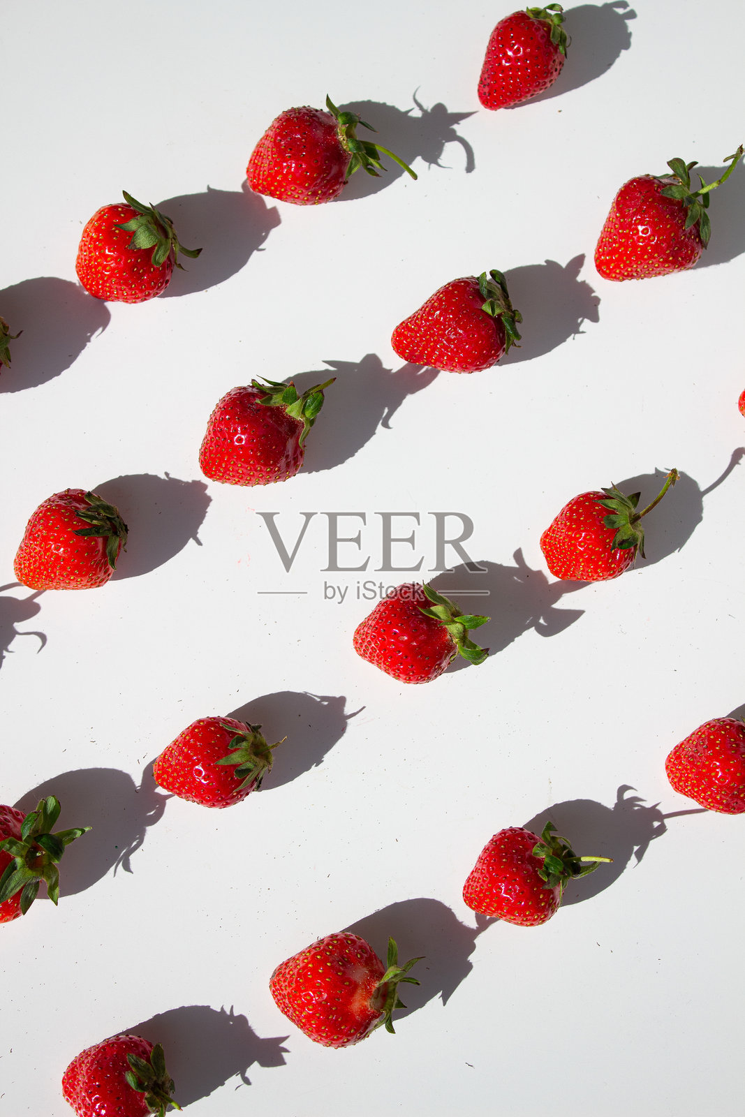 草莓在明亮的白色表面上以俏皮的线条排列。照片摄影图片