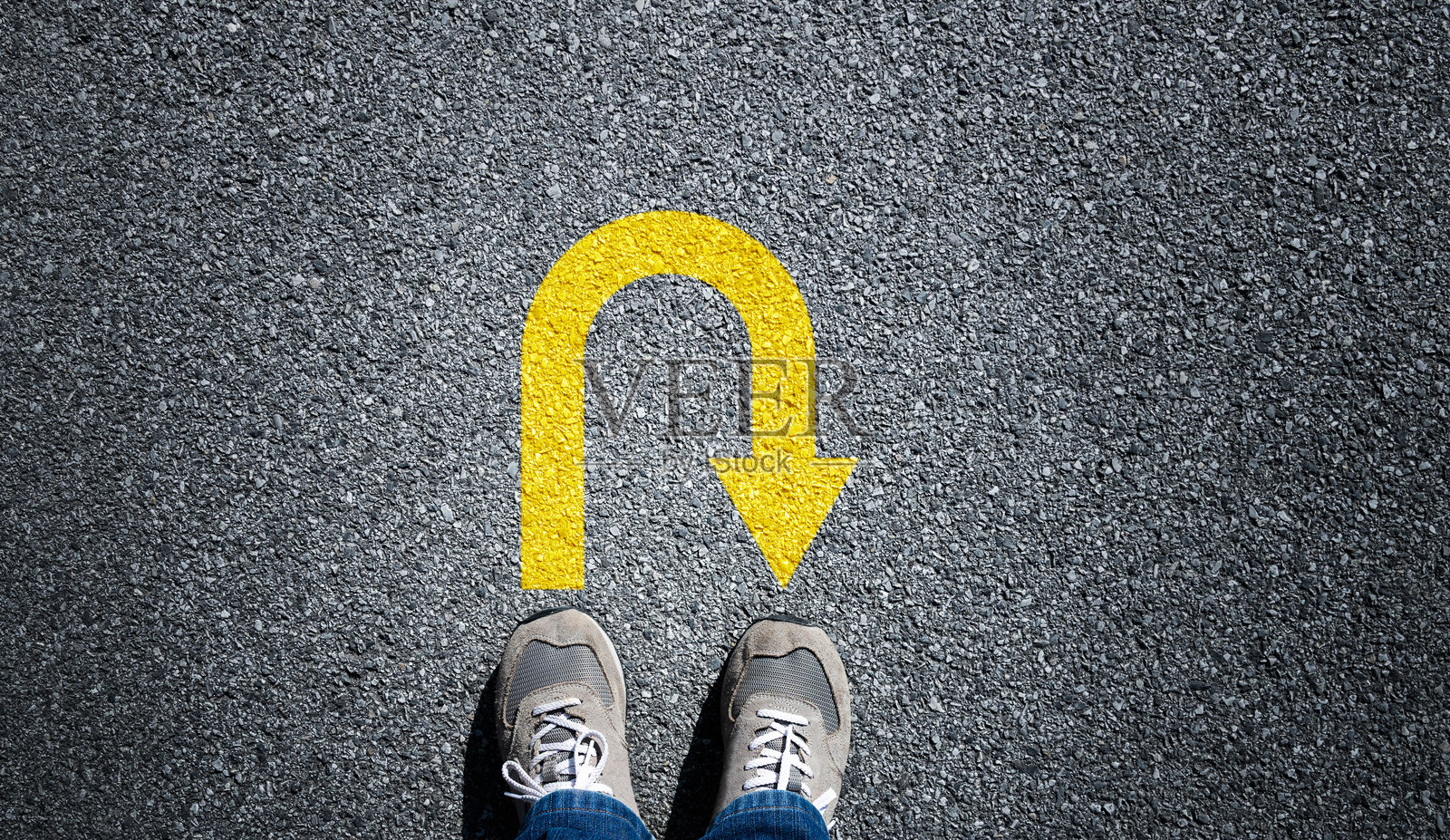 从上方俯视一名男子的双脚，站在掉头箭头标志前照片摄影图片