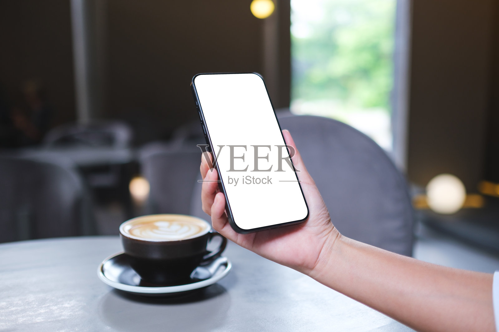 女性在咖啡馆中手持手机并使用，桌面屏幕为空白的模拟图像照片摄影图片