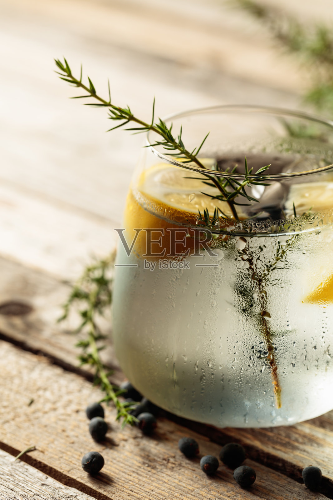 带有柠檬、杜松枝和冰块的酒精饮料（琴汤尼鸡尾酒）放在质朴的木桌上。照片摄影图片