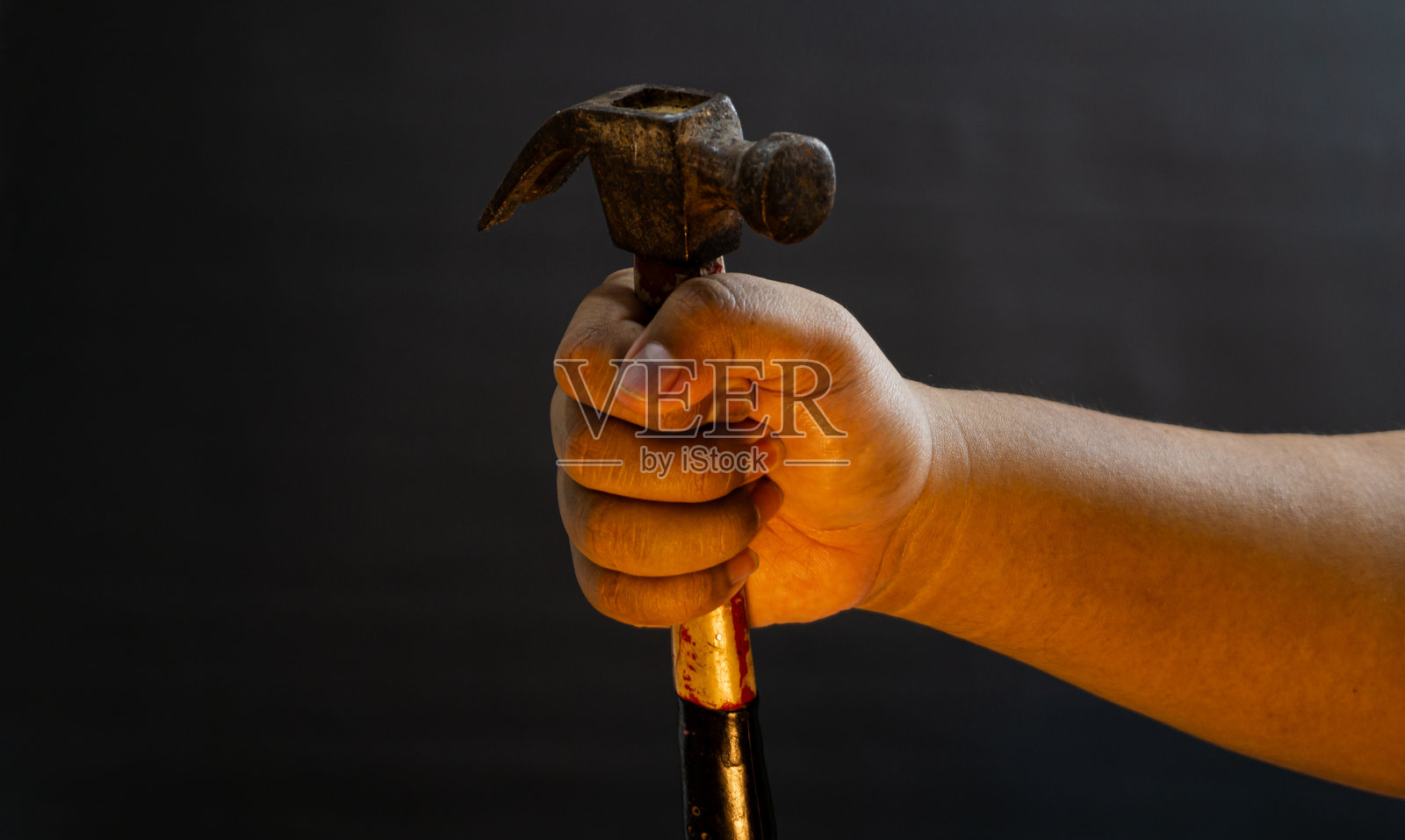 一只手握住金属锤头下方的锤子，孤立在黑色背景上，非常适合修理、建筑或维护的图像。照片摄影图片