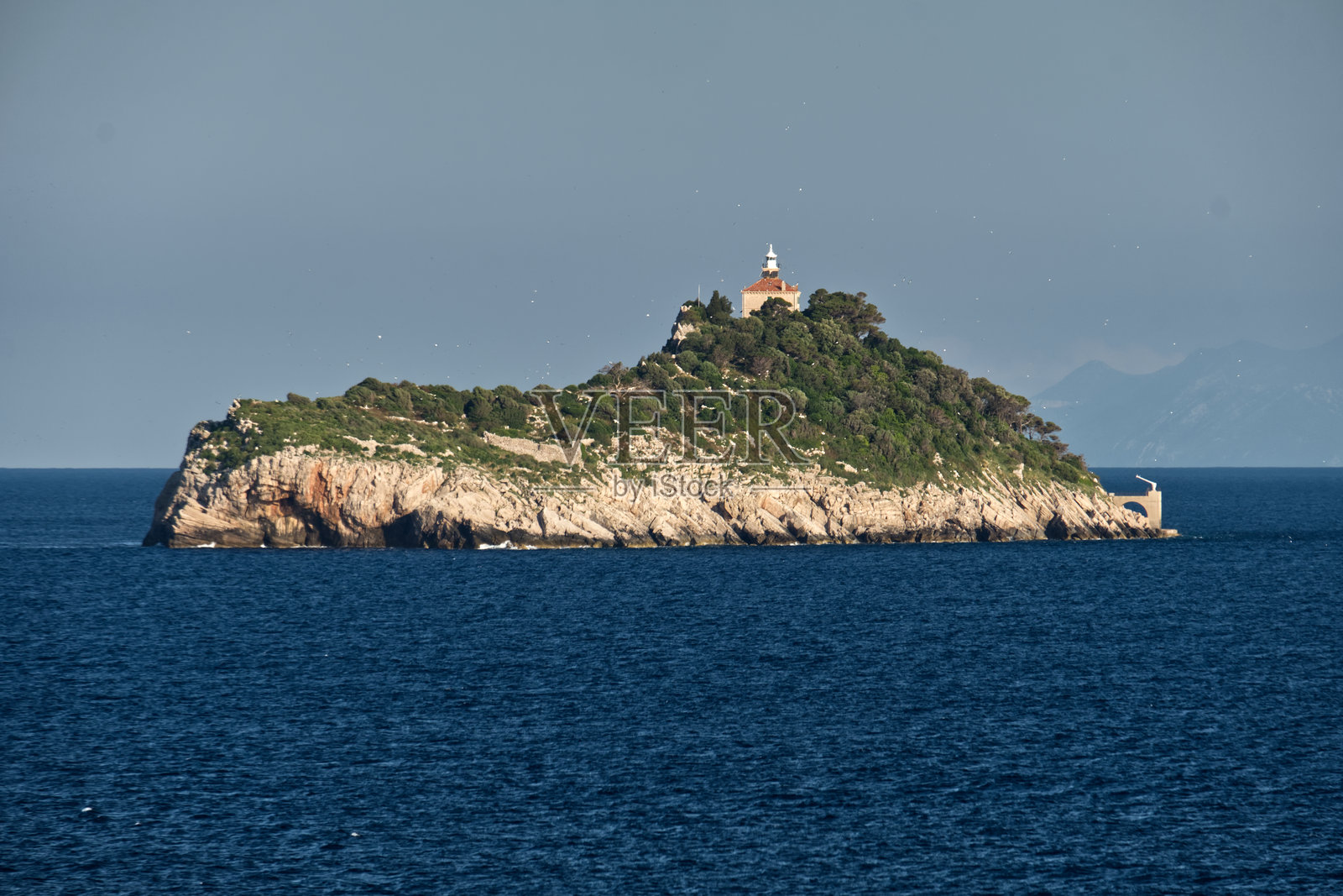 克罗地亚达尔马提亚日出时的杜布罗夫尼克群岛、灯塔和远处的山脉，海上视角照片摄影图片