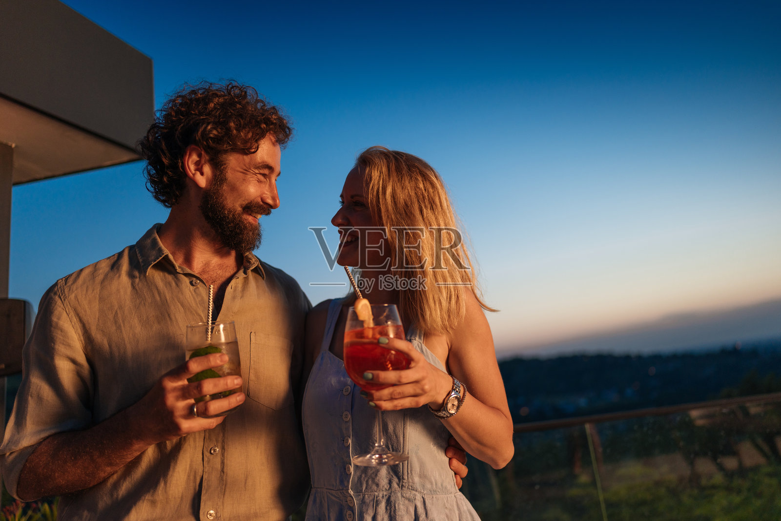 情侣在日落时分的屋顶上享用鸡尾酒照片摄影图片