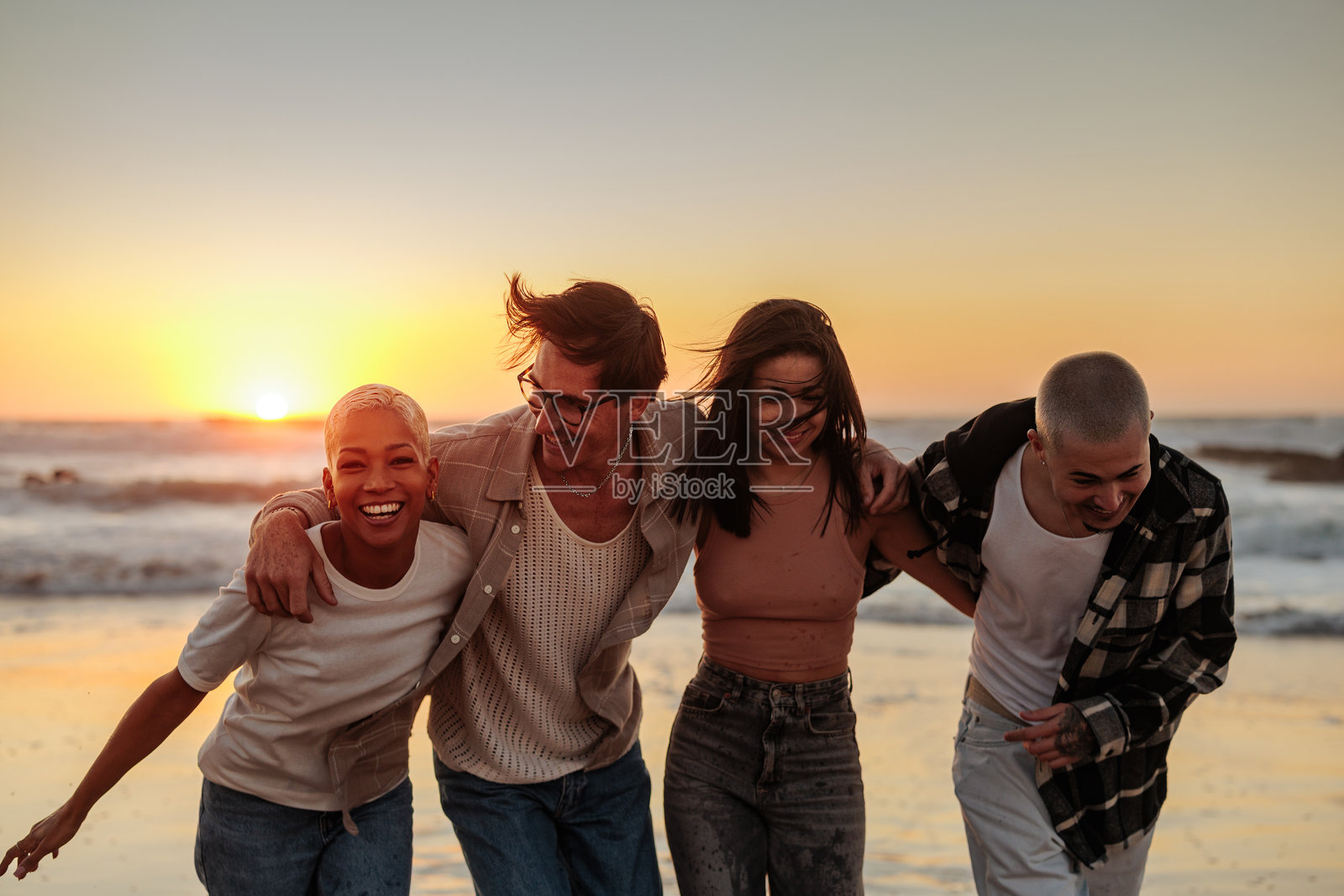 快乐的朋友们在日落时分的海滩上散步，享受夏季假期照片摄影图片