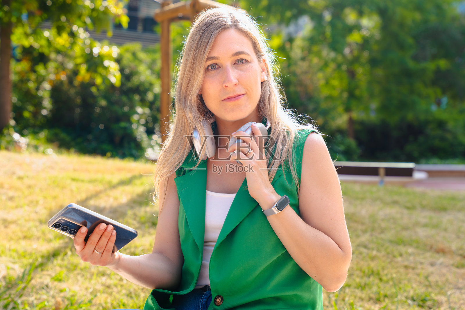 在公园户外戴着耳机的女性手持智能手机并看向镜头照片摄影图片