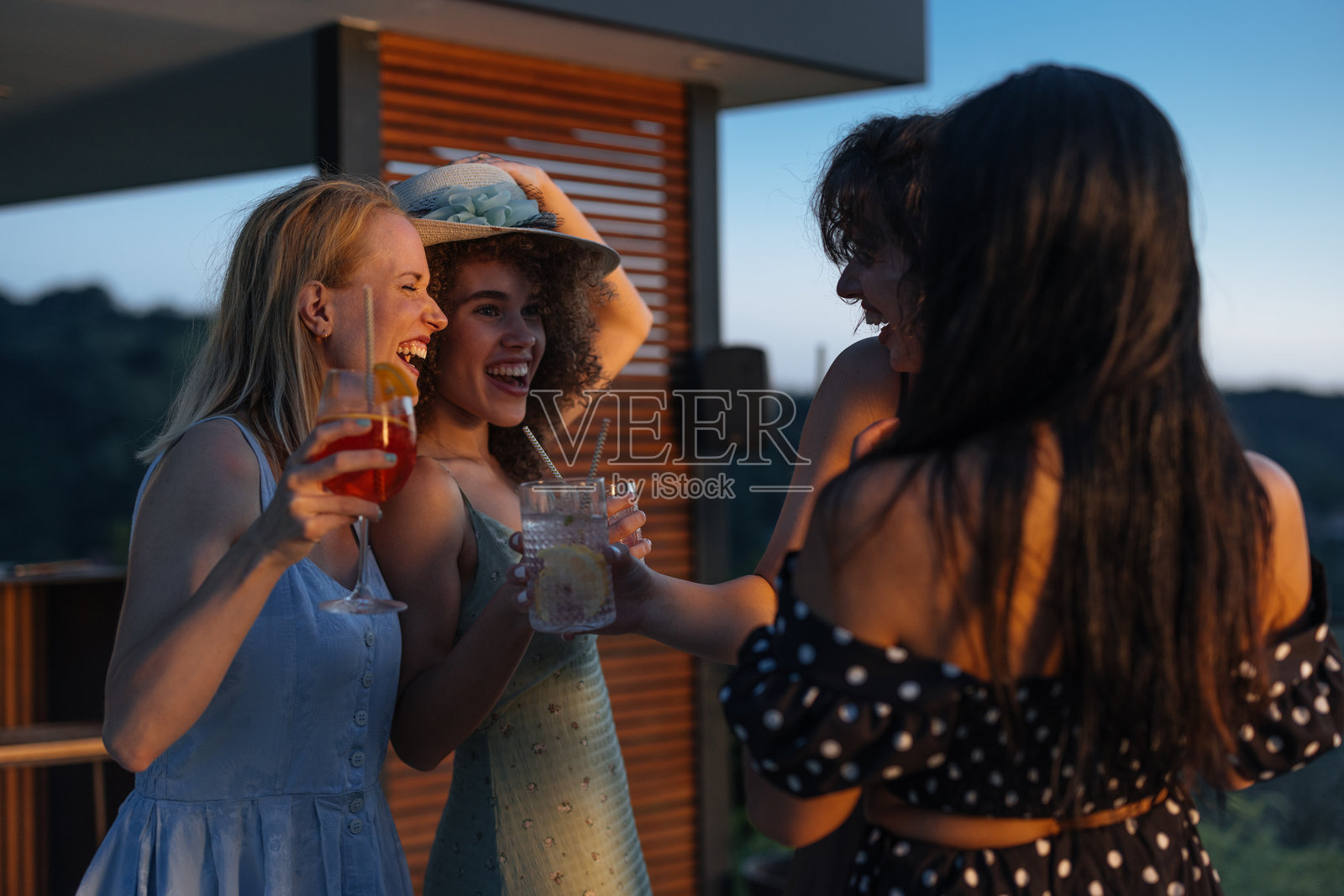 四位快乐的年轻女性在日落派对上欢笑并饮用鸡尾酒照片摄影图片