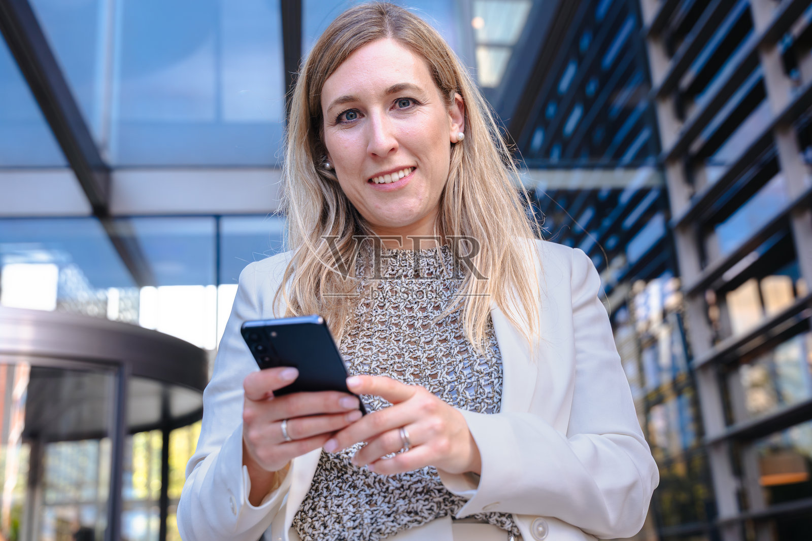 户外的女商人使用智能手机，现代玻璃建筑，城市。照片摄影图片