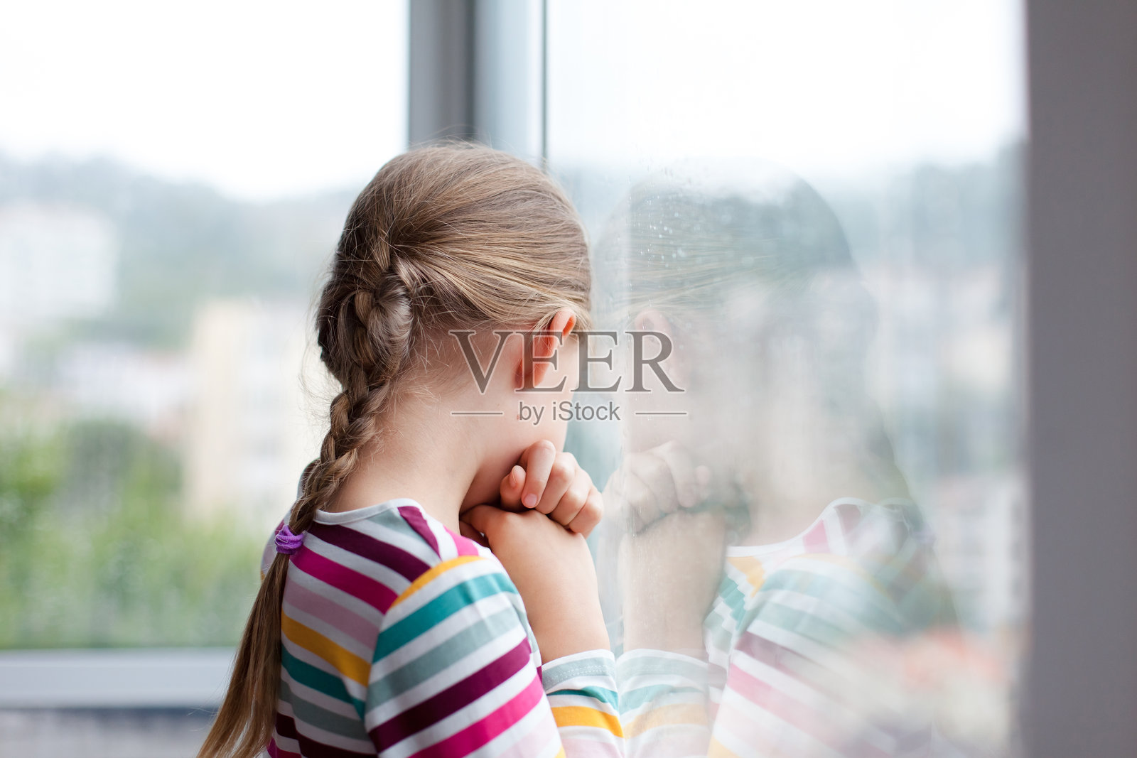 伤心的孩子透过雨窗望向家外。在隔离期间，感到沮丧的孩子独自一人。照片摄影图片