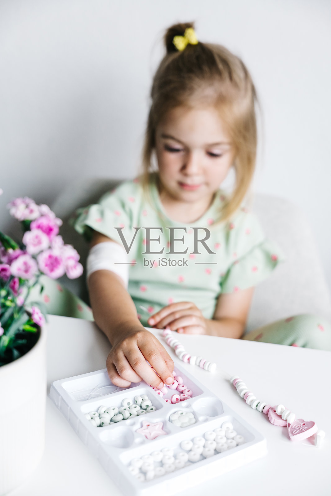 年轻女孩在家中进行创意串珠活动，周围有五颜六色的珠子和花朵。照片摄影图片