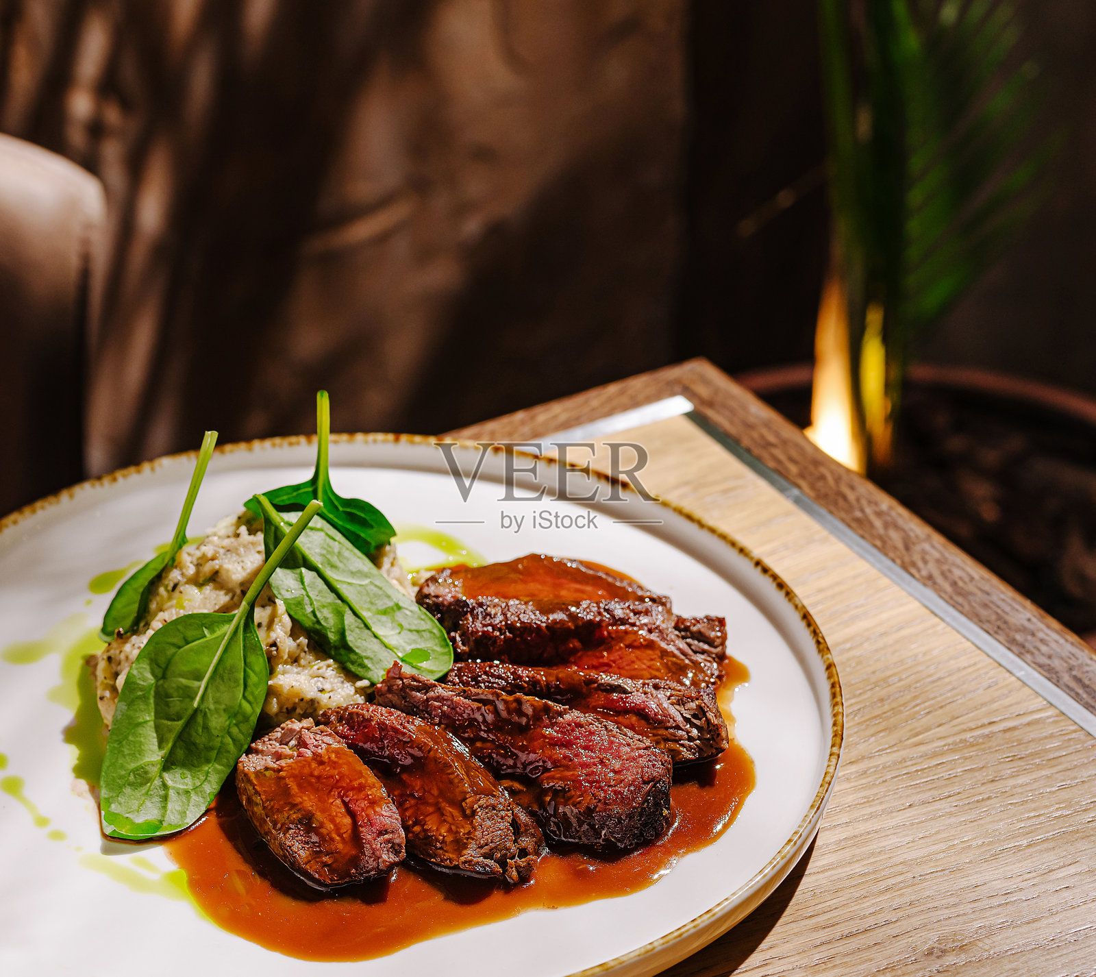 美味的牛肉菜肴，搭配菠菜和奶油酱，室内享用。照片摄影图片
