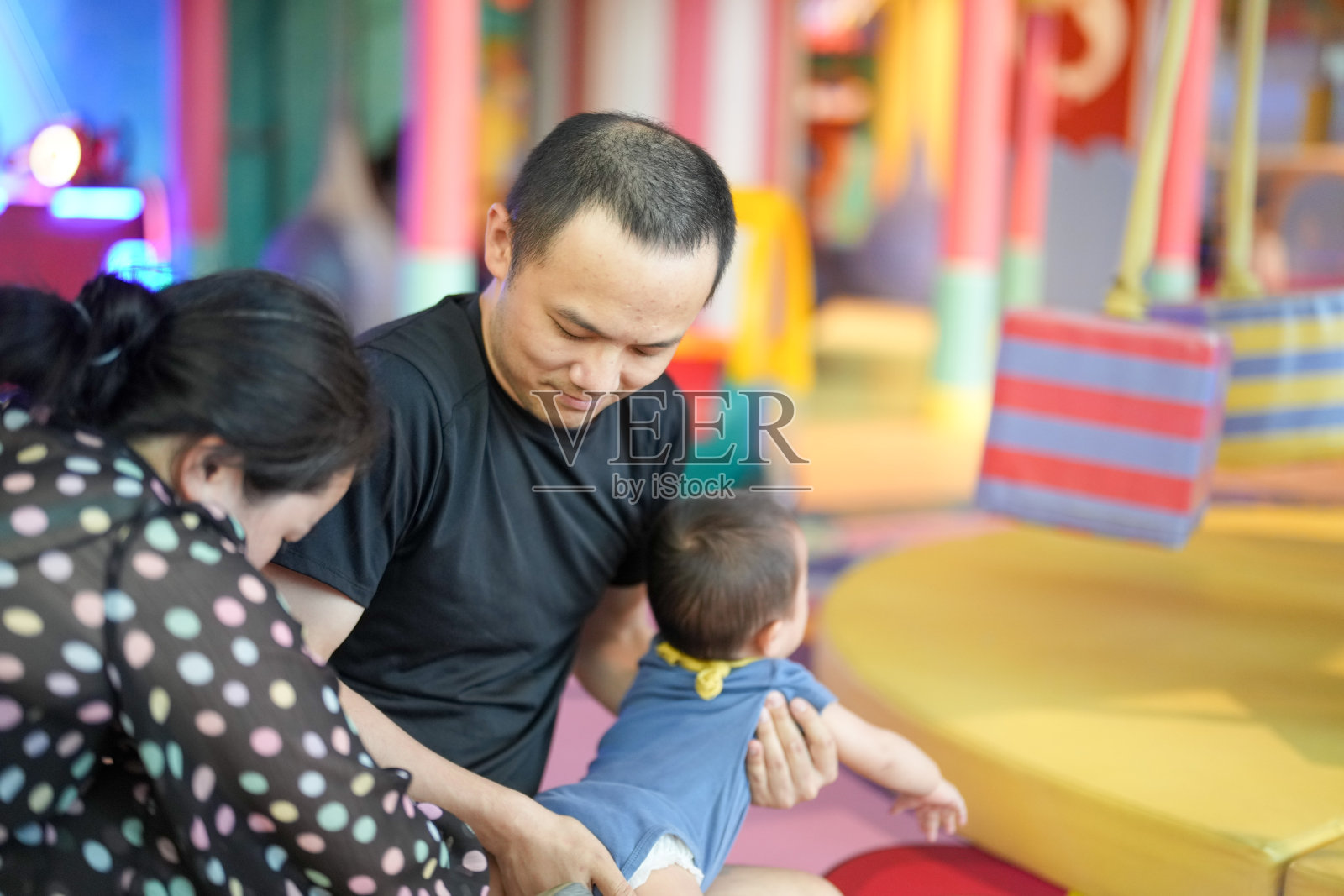 在室内游乐区，父母帮助一岁的小孩换衣服。中国上海。春天。照片摄影图片