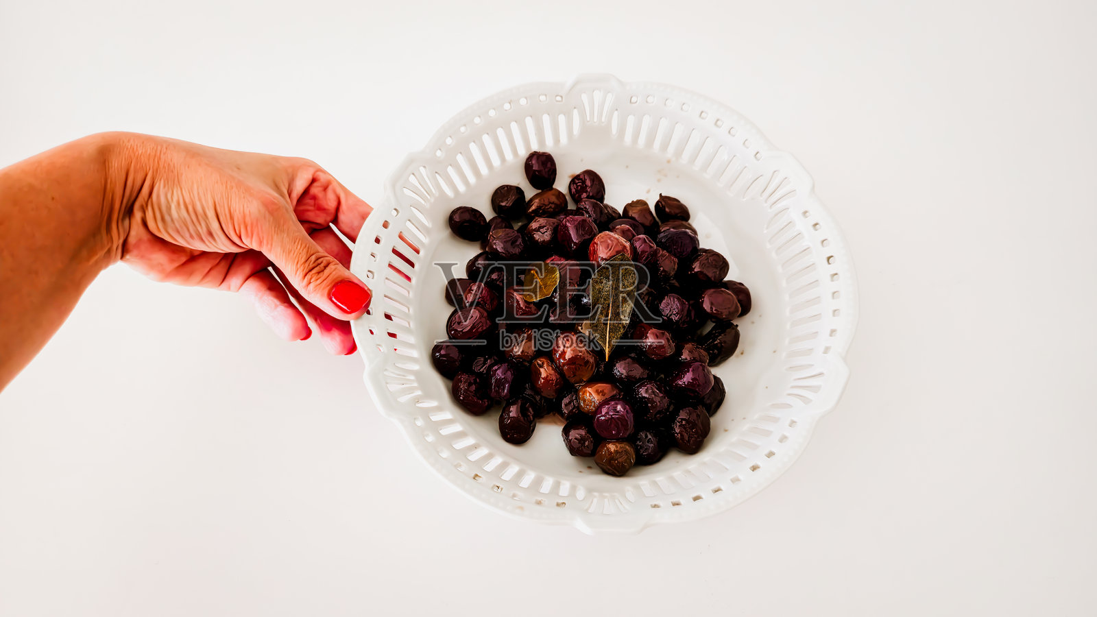 白色背景下的白色陶瓷碗中盛放着腌制黑橄榄和月桂叶照片摄影图片