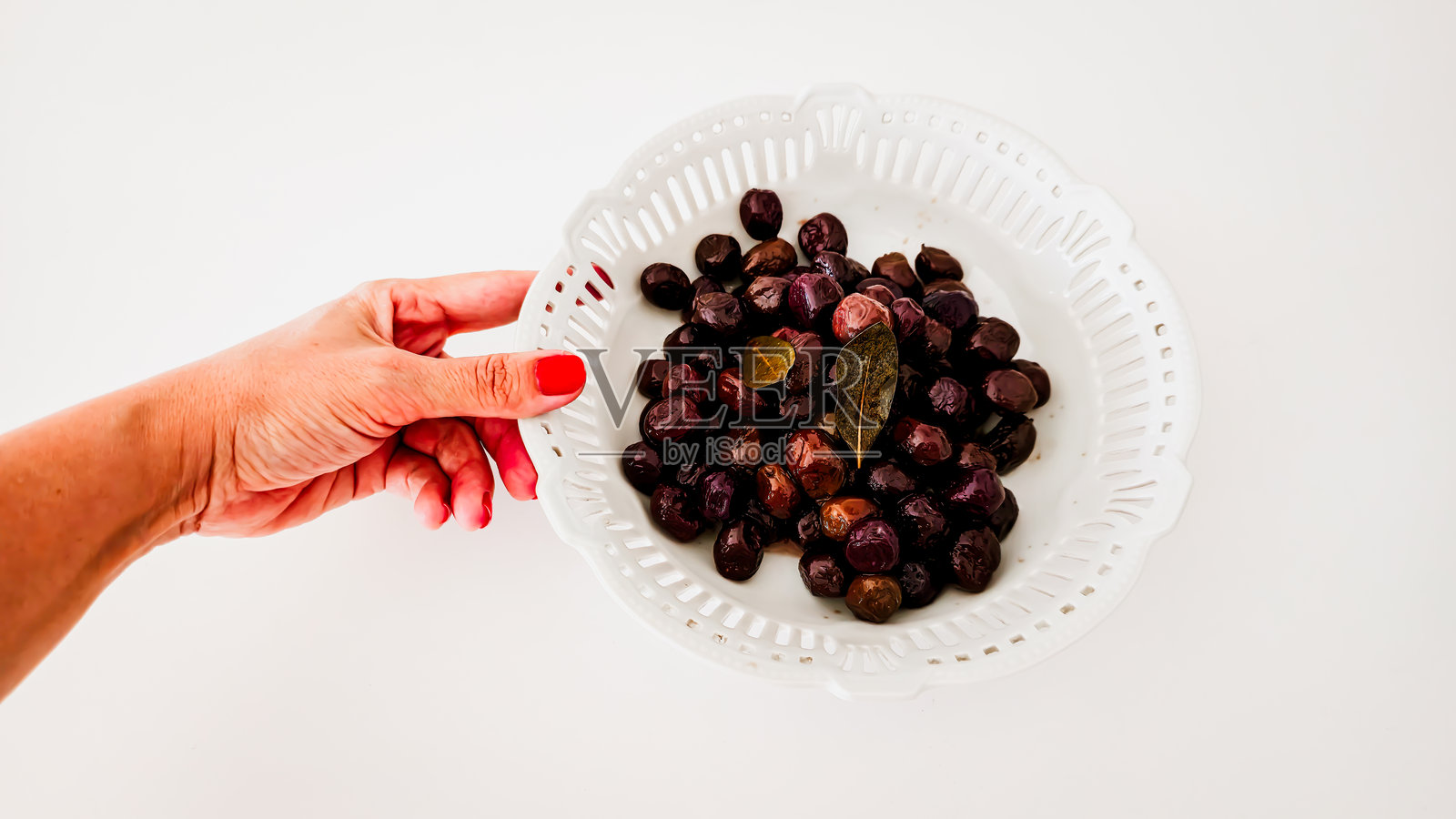 白色背景下的白色陶瓷碗中盛放着腌制黑橄榄和月桂叶照片摄影图片