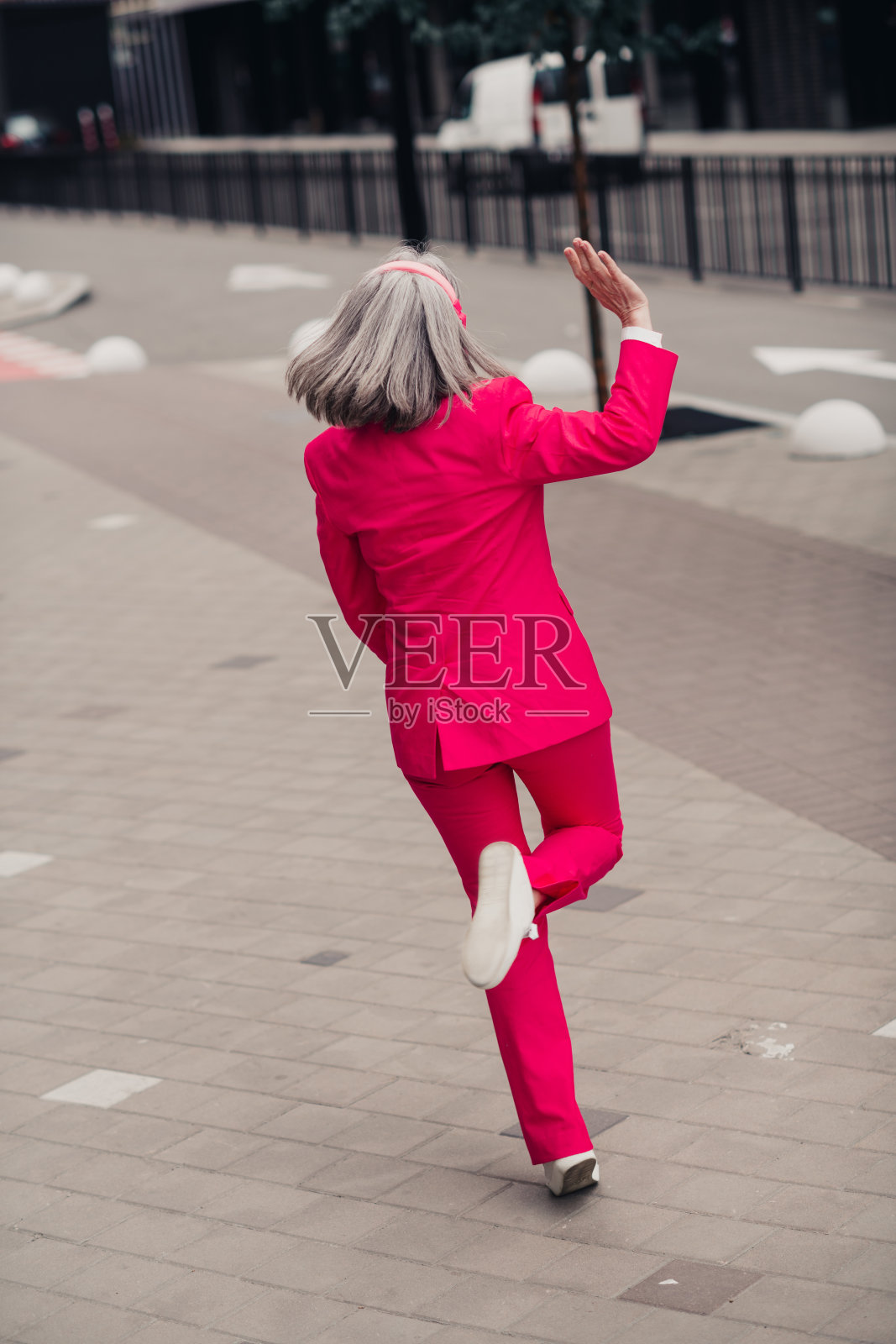 优雅的老年女性穿着鲜艳的粉色西装，自信地走在白天的城市街道上照片摄影图片