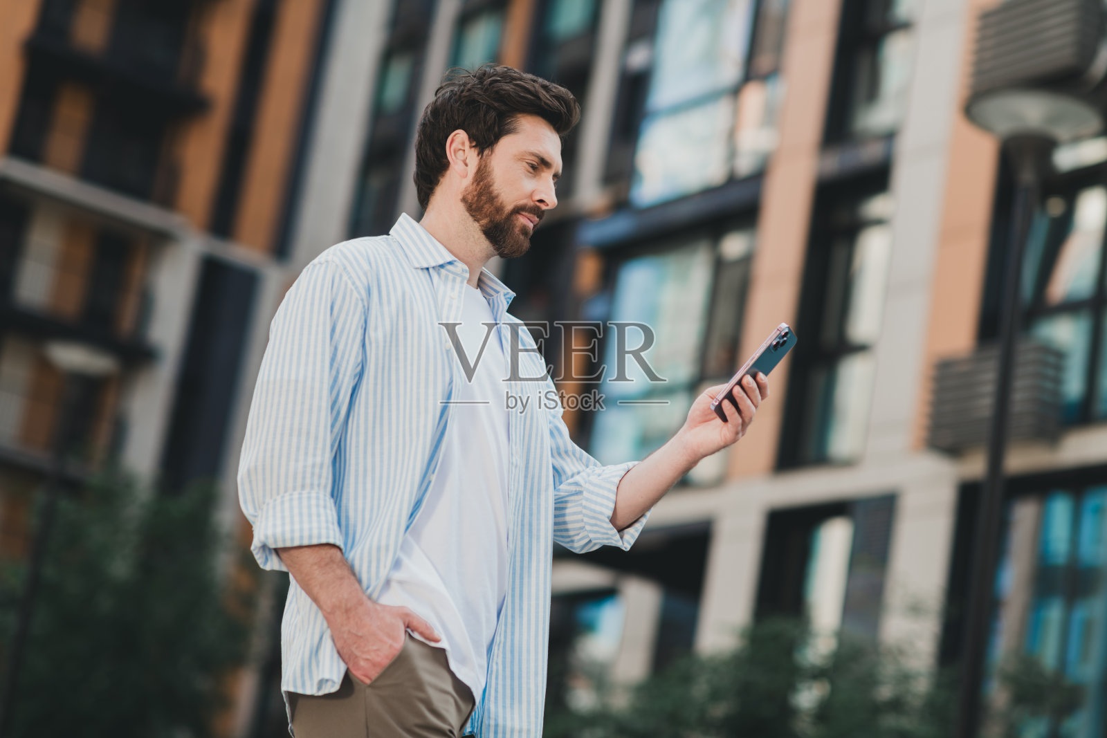 年轻帅气的男子在现代城市环境中悠闲地散步时查看智能手机照片摄影图片