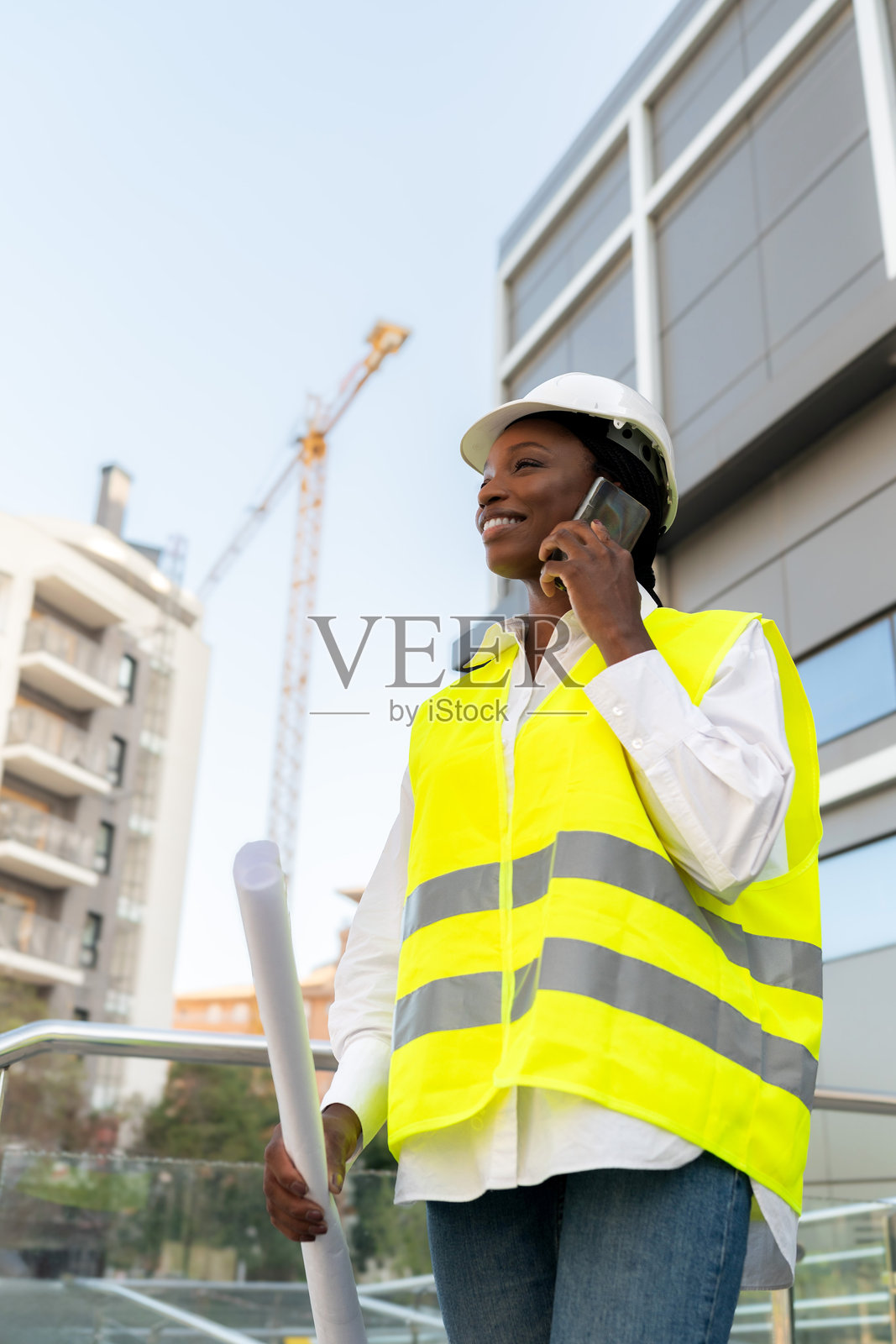 身穿安全帽和安全背心的非裔美国女性工程师在建筑工地上打电话照片摄影图片