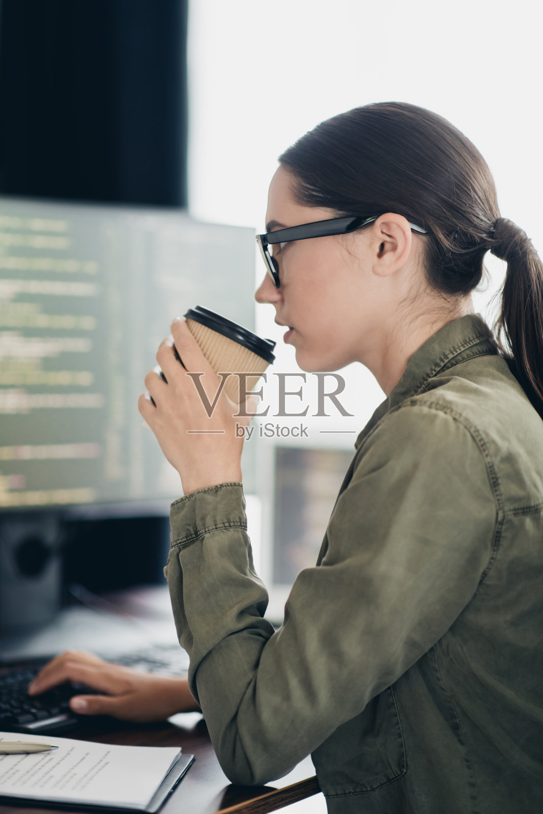 年轻的职业女性在现代工作空间中一边喝咖啡一边远程工作，担任计算机程序员。照片摄影图片