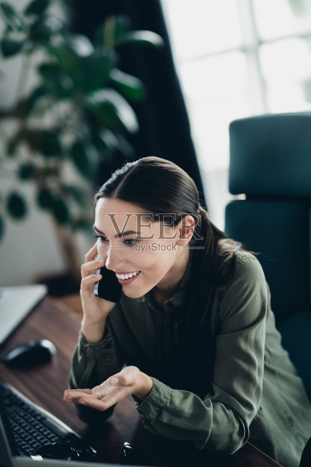 愉快的年轻职业女性在时尚的办公室环境中一边打电话一边使用电脑工作照片摄影图片