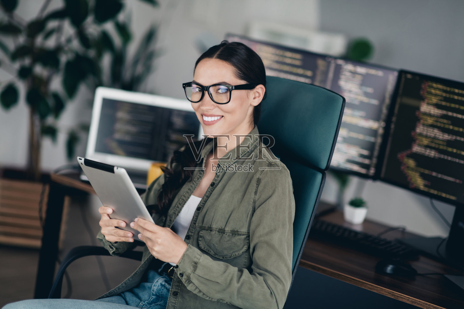 自信的女性程序员在现代办公室环境中使用平板电脑远程工作，周围有多台显示器。照片摄影图片