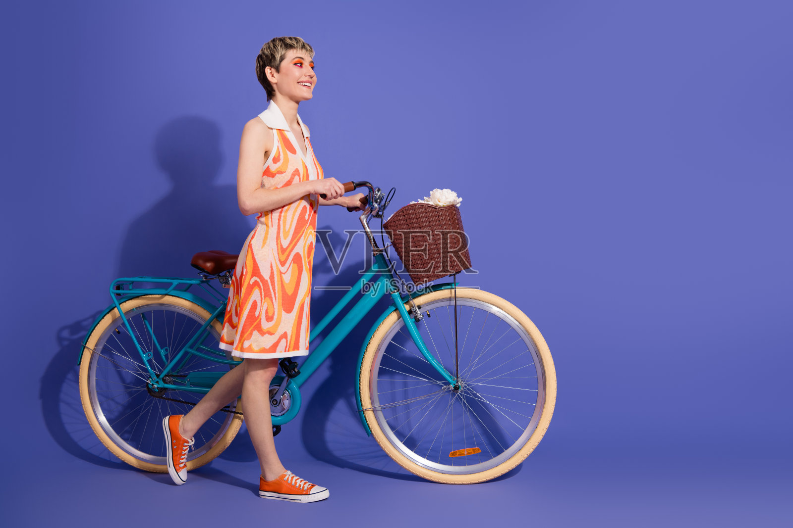 时尚年轻女性穿着鲜艳的裙子，骑着复古自行车，背景为紫色，享受闲暇时光。照片摄影图片