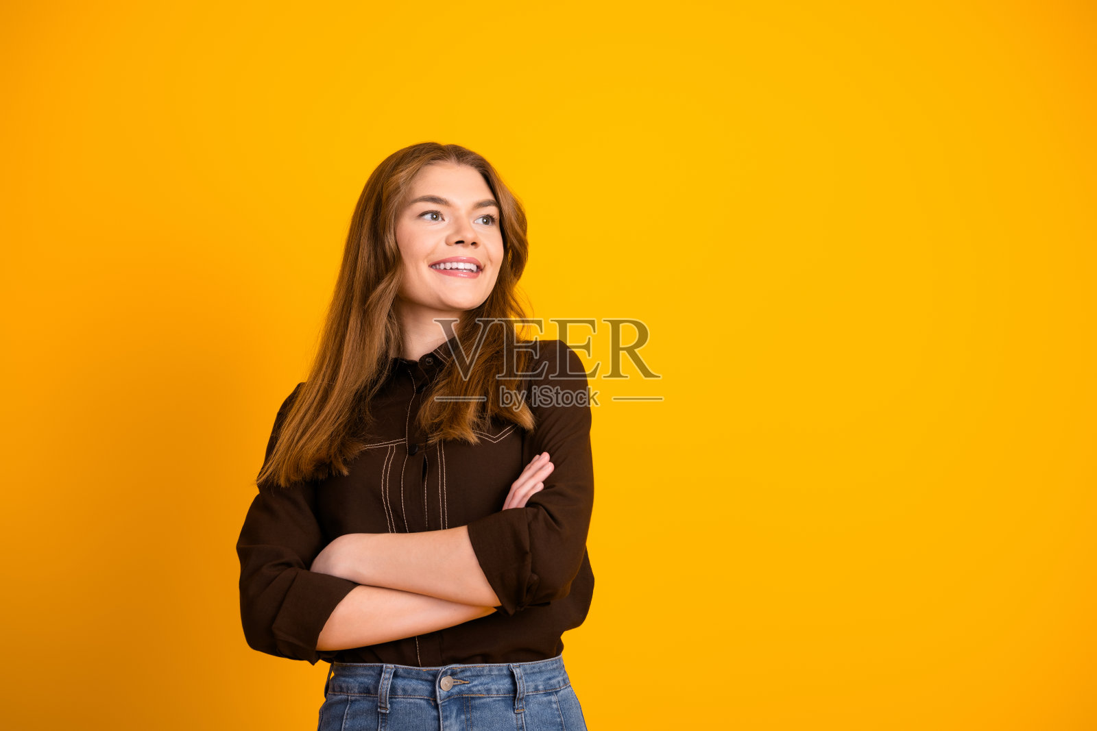 穿着休闲服的积极年轻女性，双臂交叉，站在黄色背景前，展现自信与魅力。照片摄影图片