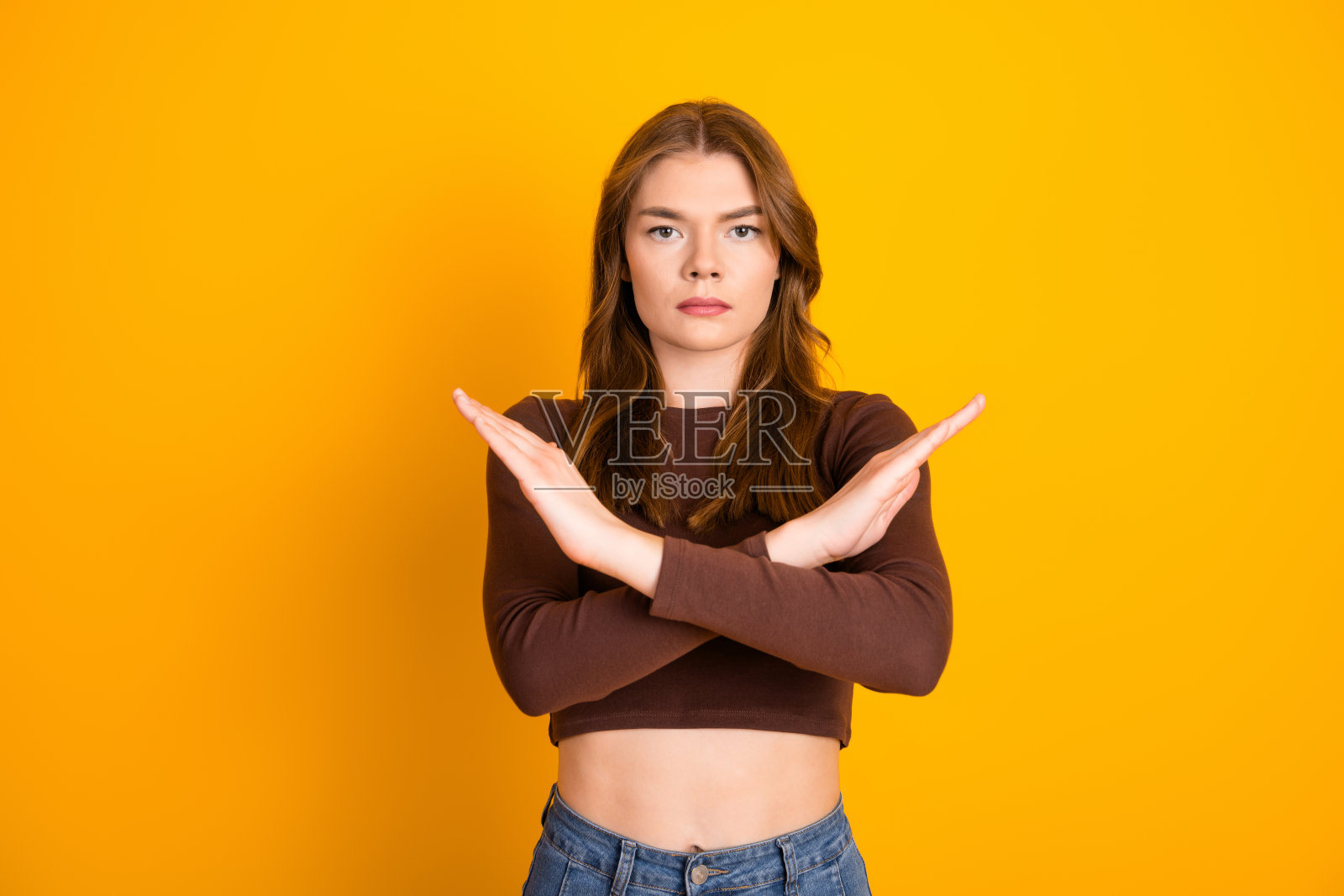 自信的年轻女性双臂交叉，面露严肃表情，背景为纯黄色。照片摄影图片