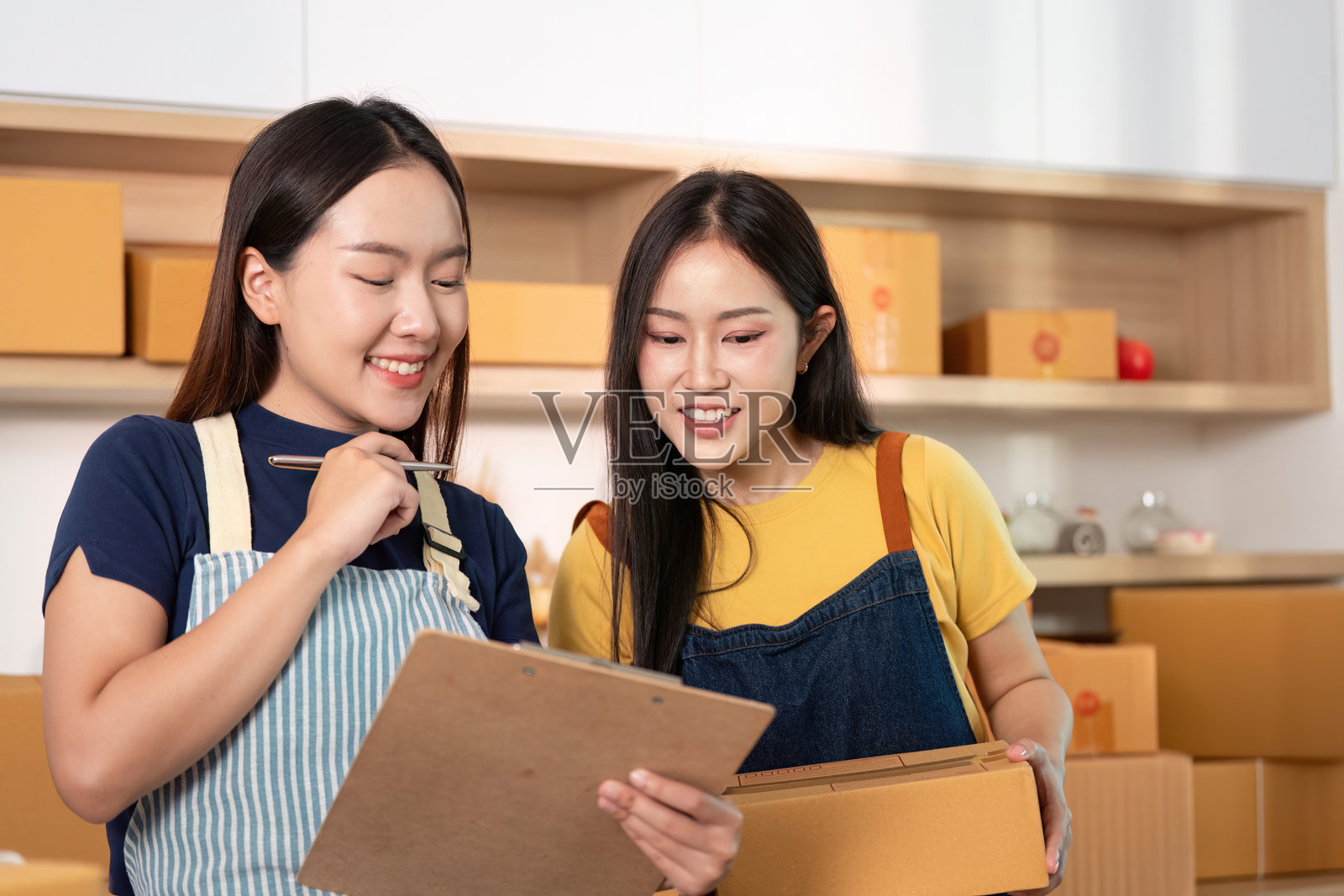 商业合作。两位女性正在查看项目细节，手持夹板和箱子。照片摄影图片