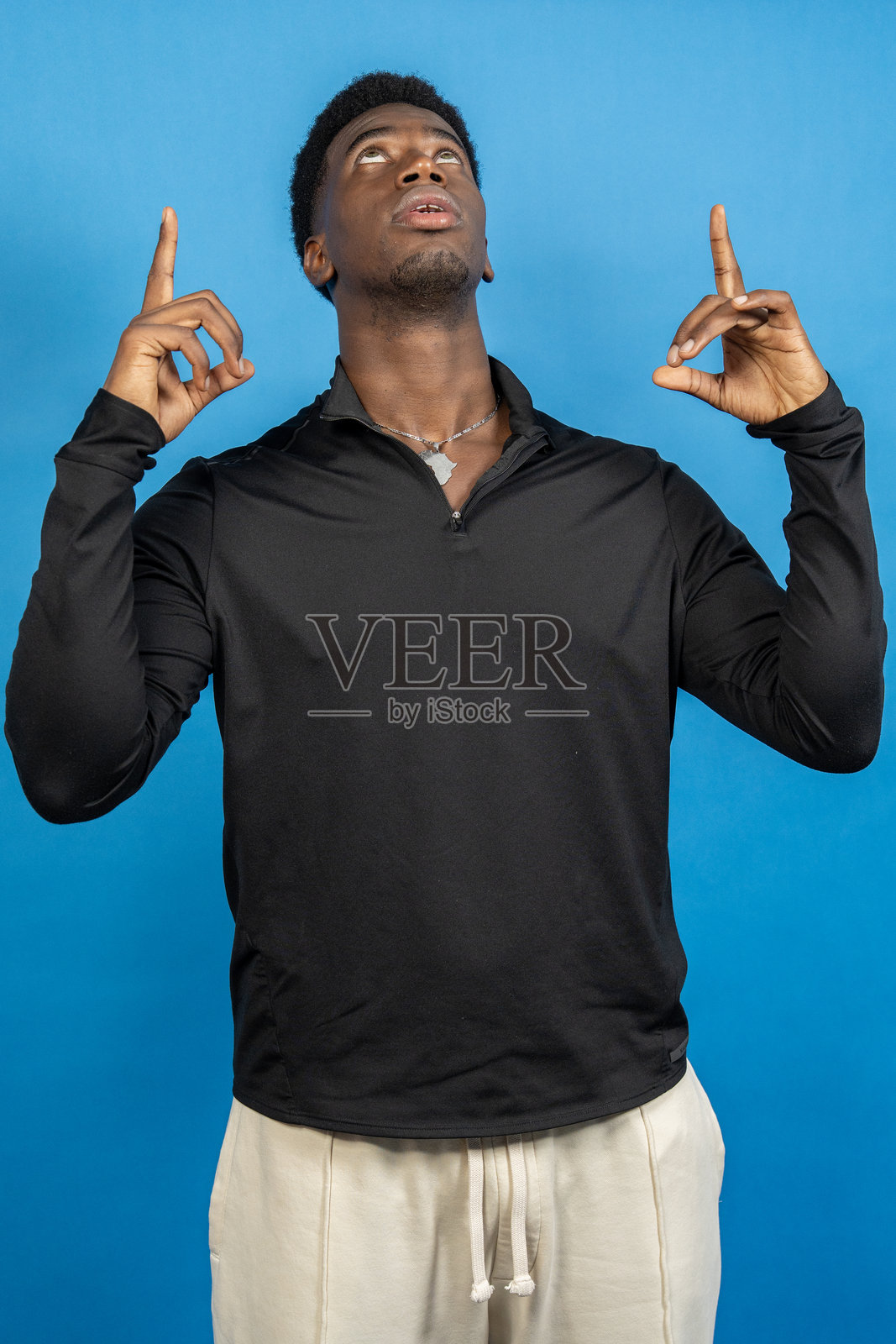 年轻男子在蓝色背景下用食指指向上方照片摄影图片